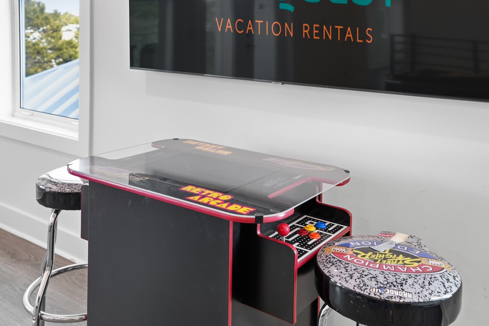 120 Dune Drive – Game table with retro arcade machine and two bar stools in a bright room with large windows.