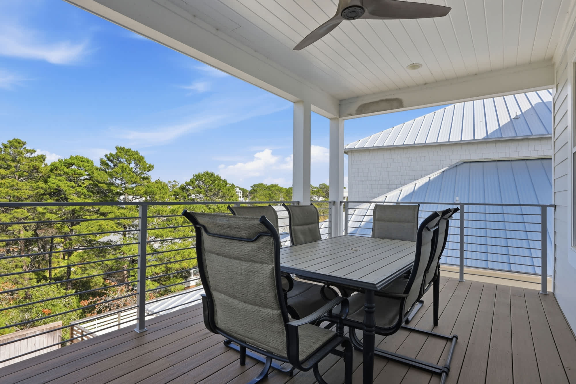 120 Dune Drive – Covered balcony with a dining table and chairs overlooking trees and blue sky.