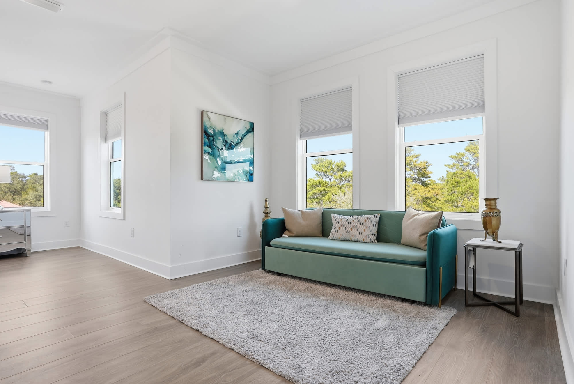 120 Dune Drive – Bright living room with teal sofa, large windows, and a soft rug.