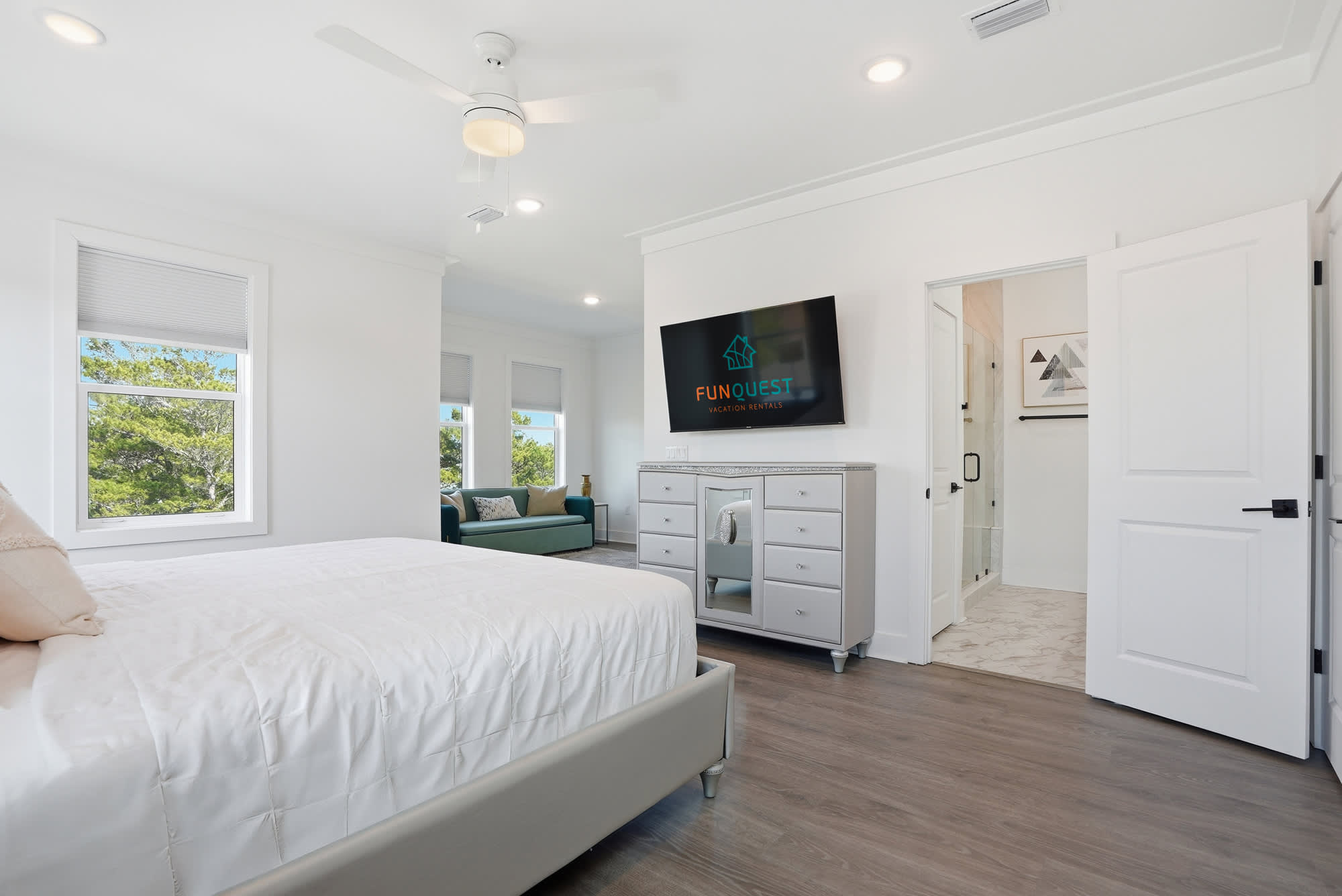 120 Dune Drive – Bright bedroom with a large bed, mounted TV, dresser, and access to a bathroom.