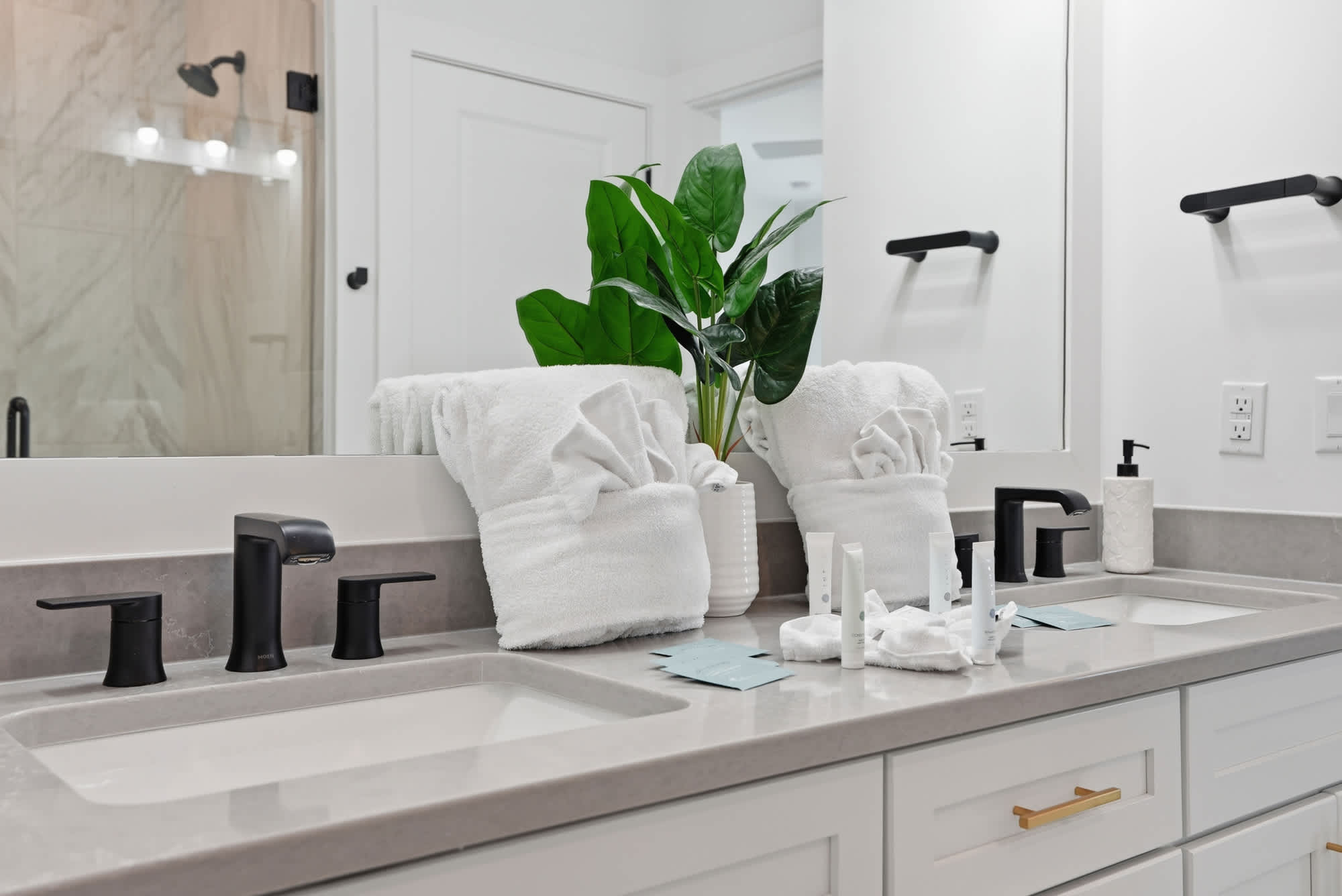 120 Dune Drive – Modern bathroom with double sinks, black fixtures, plush towels, and a potted plant.