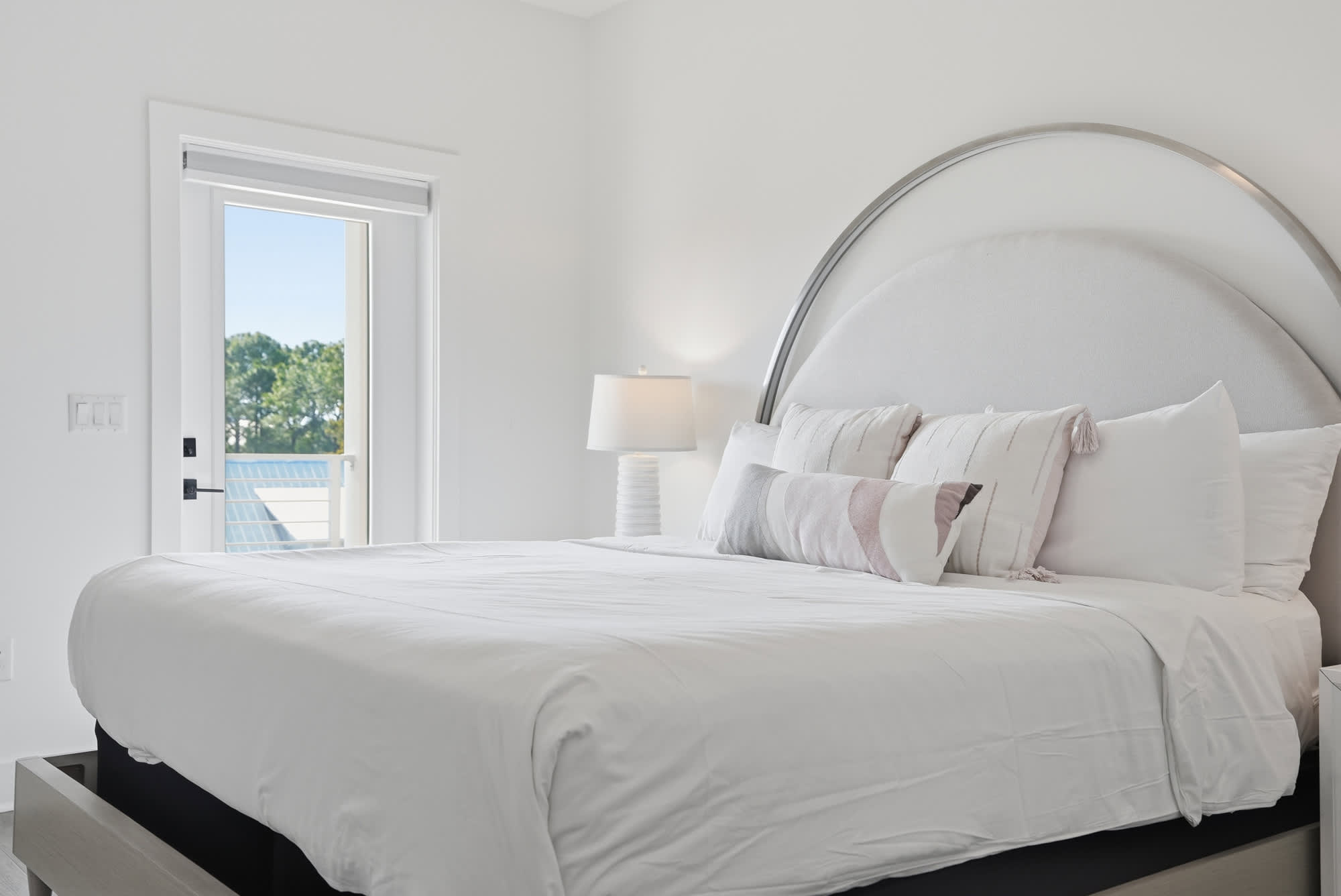 120 Dune Drive – Bright bedroom with a large bed, bedside lamp, and sliding door showing greenery outside.