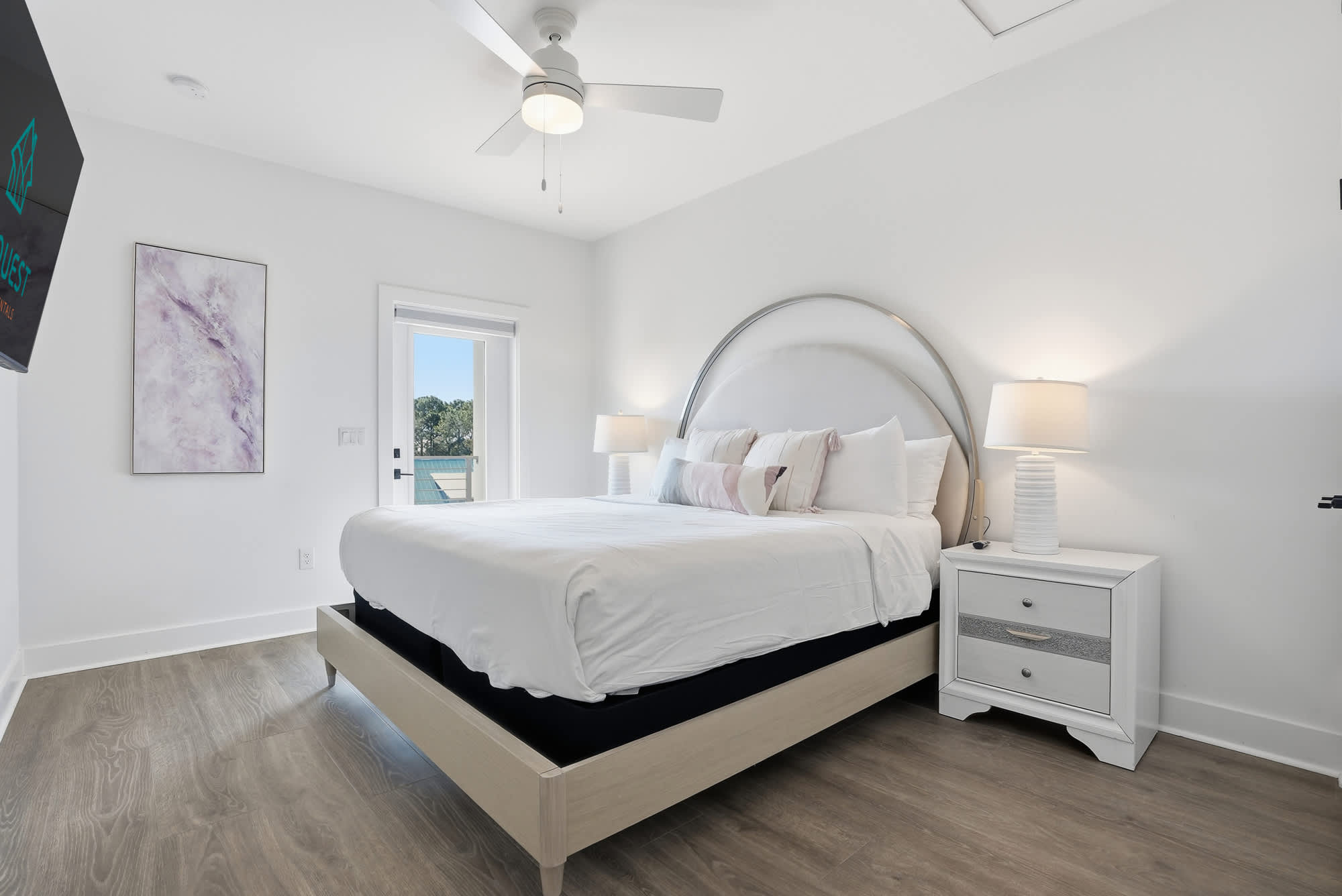 120 Dune Drive – Bright bedroom with a large bed, nightstand, window, and a wall-mounted TV.