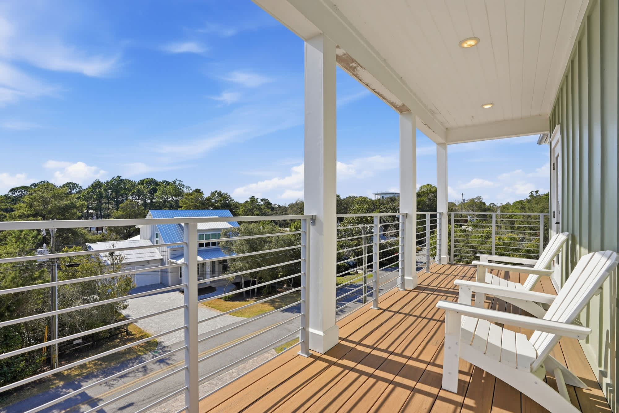 120 Dune Drive – Balcony with two white chairs overlooking trees and nearby houses under a blue sky.