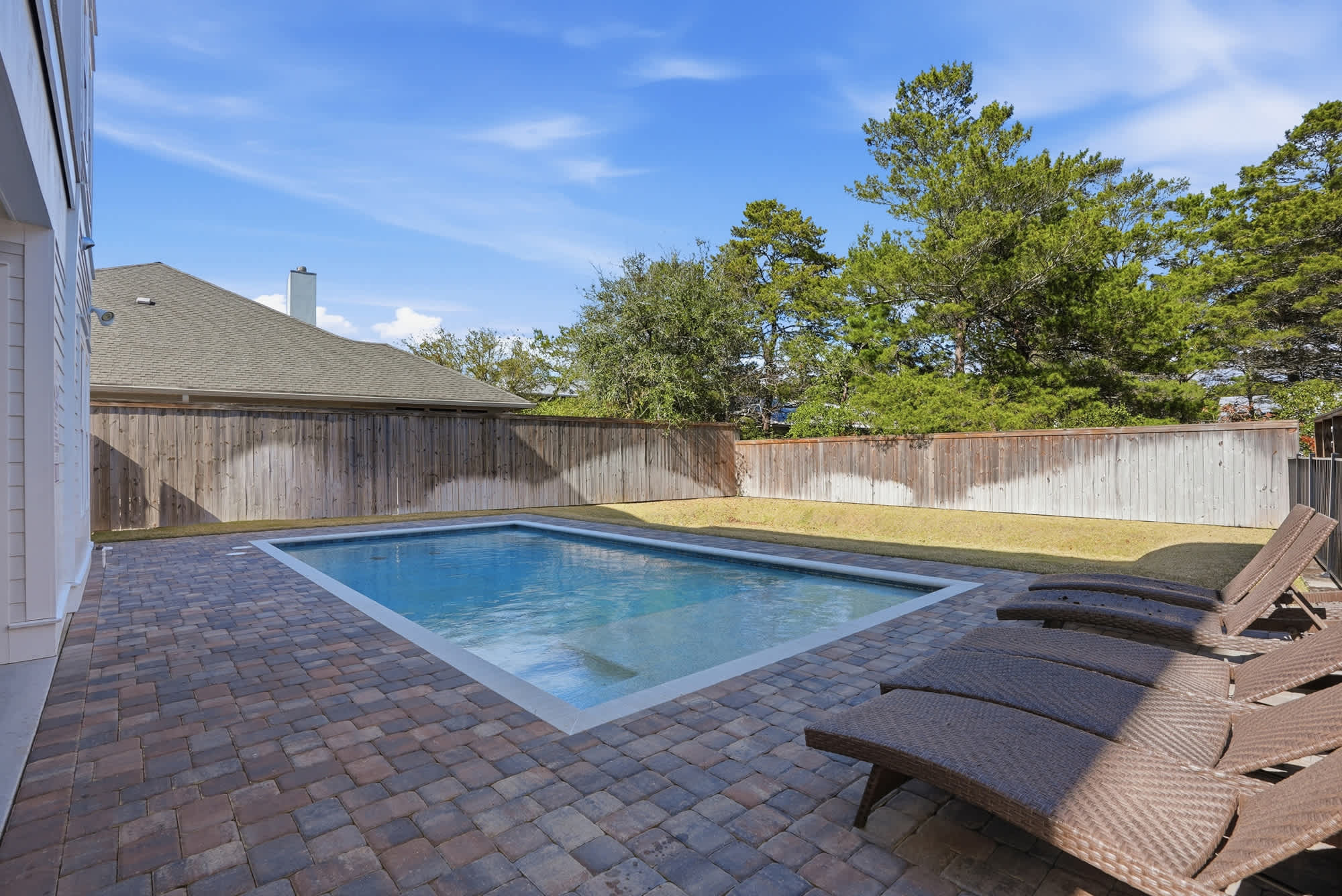 120 Dune Drive – Backyard with a swimming pool, brick patio, and lounge chairs, surrounded by a wooden fence and trees.
