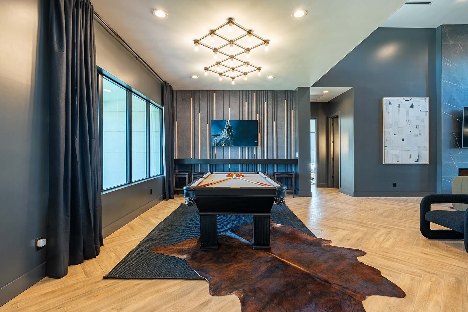 Stylish entertainment space featuring a sleek pool table, modern lighting, and a cozy seating area with a large Smart TV.