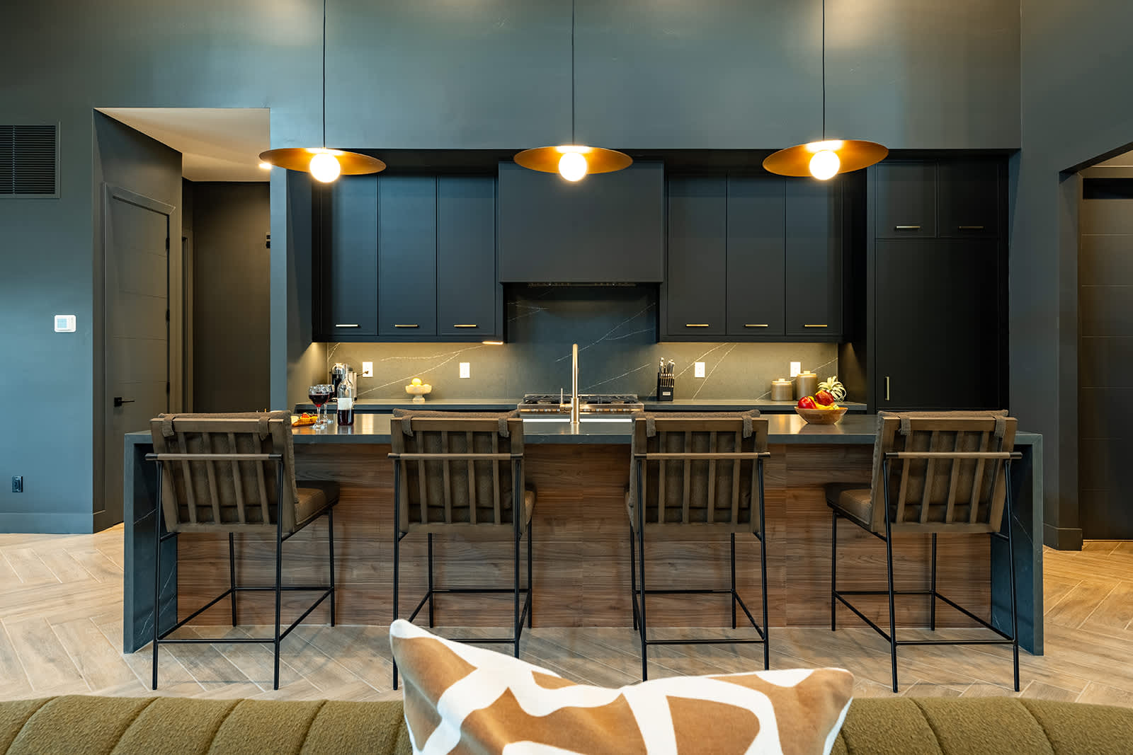 Gather in this sleek, modern kitchen featuring dark cabinetry, a spacious island with seating for four, and warm pendant lighting—perfect for casual meals or socializing.