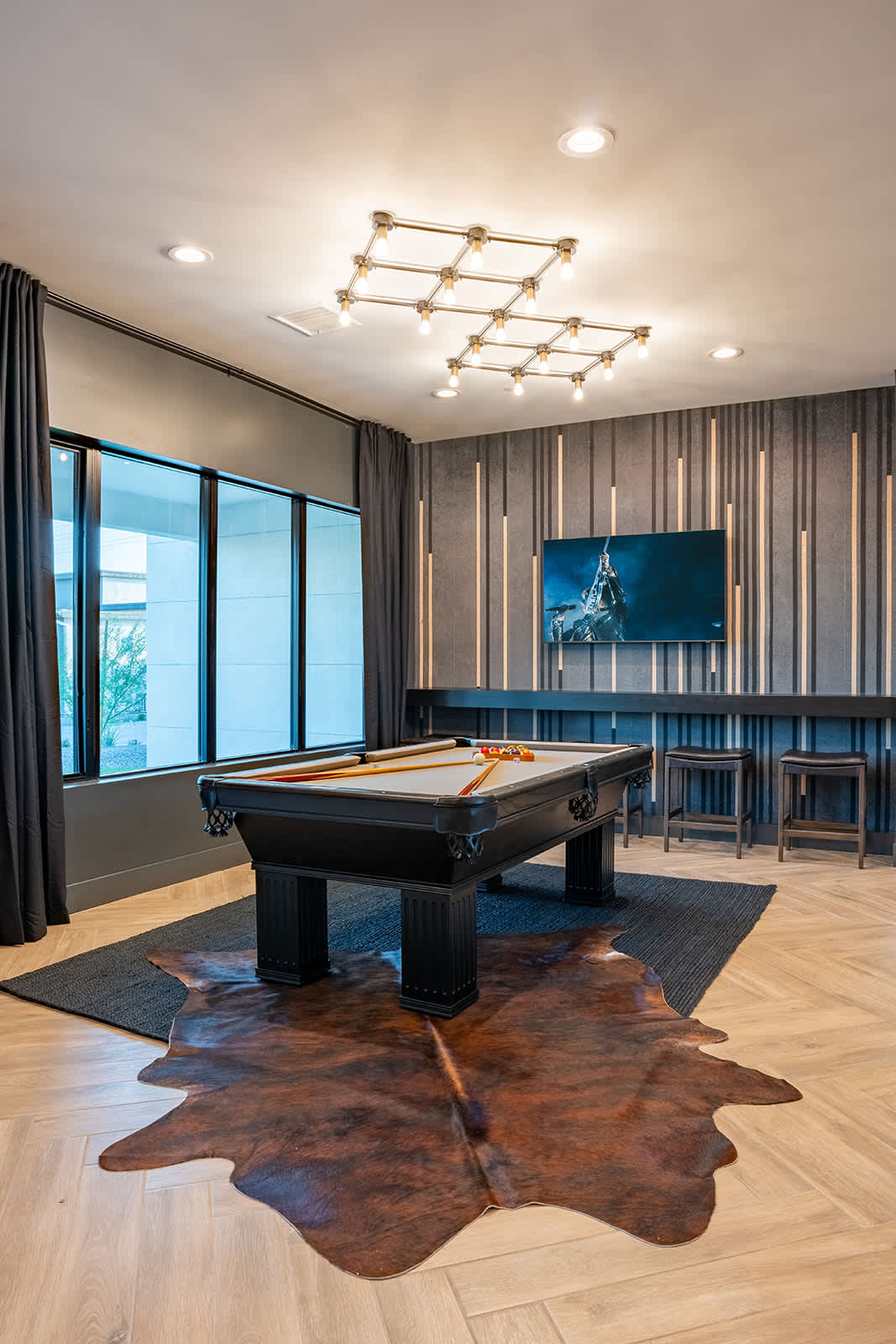 Stylish entertainment space featuring a sleek pool table, modern lighting, and a cozy seating area with a large Smart TV.