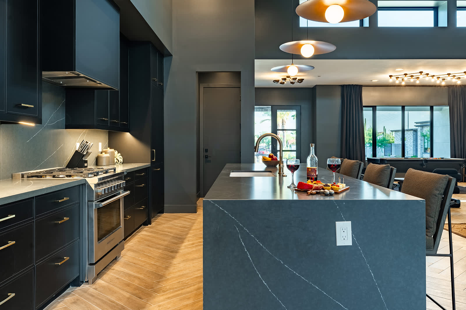 Gather in this sleek, modern kitchen featuring dark cabinetry, a spacious island with seating for four, and warm pendant lighting—perfect for casual meals or socializing.
