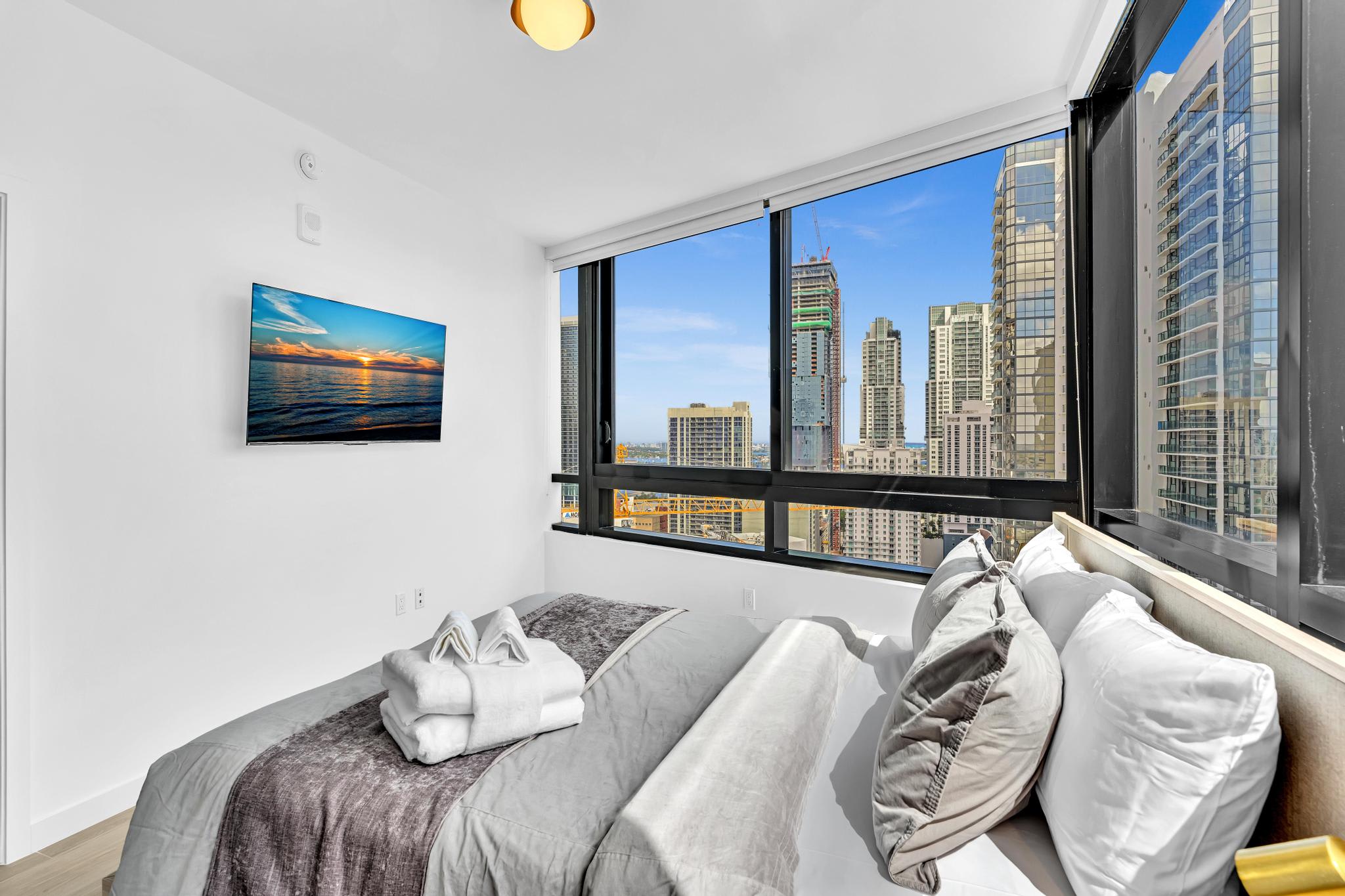 Enjoy breathtaking city views from this modern studio bedroom, featuring cozy bedding and a sleek TV for ultimate relaxation.