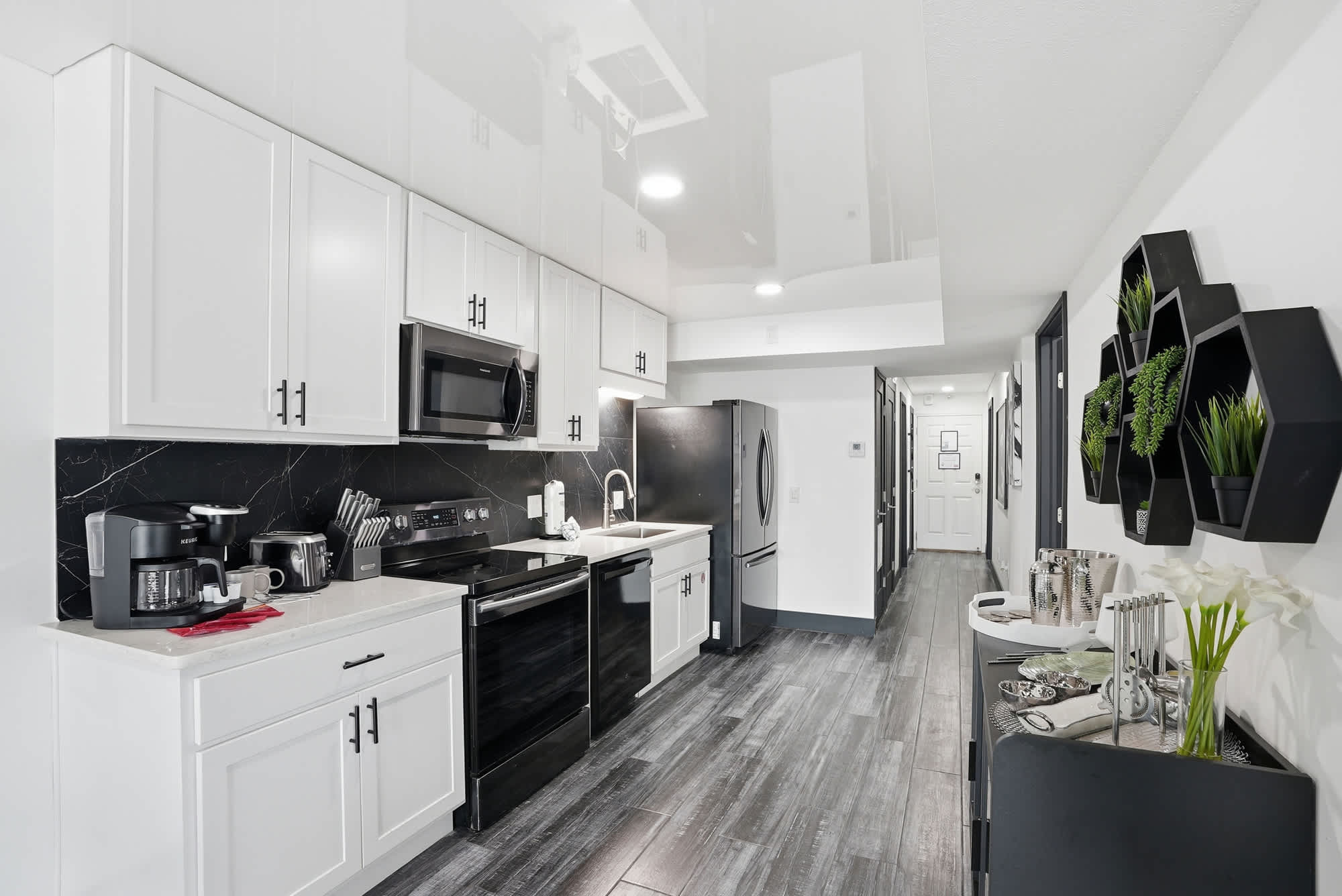 The Summit 132 – Modern kitchen with black appliances, white cabinetry, and a hallway leading to other rooms.