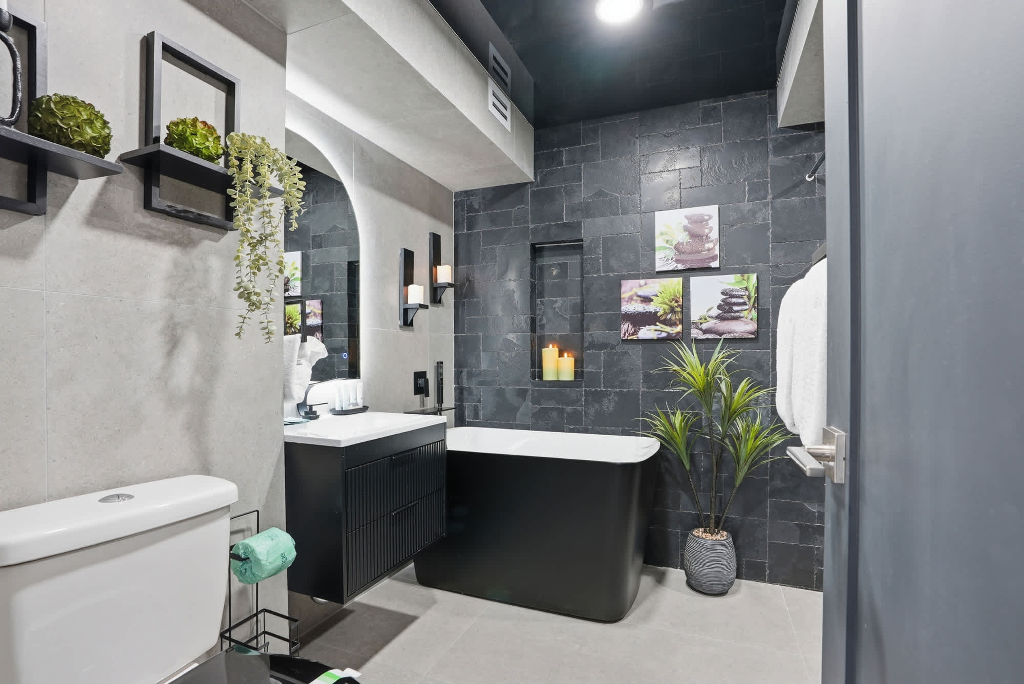 The Summit 132 – Modern bathroom with black stone walls, freestanding bathtub, vanity, and decorative plants.