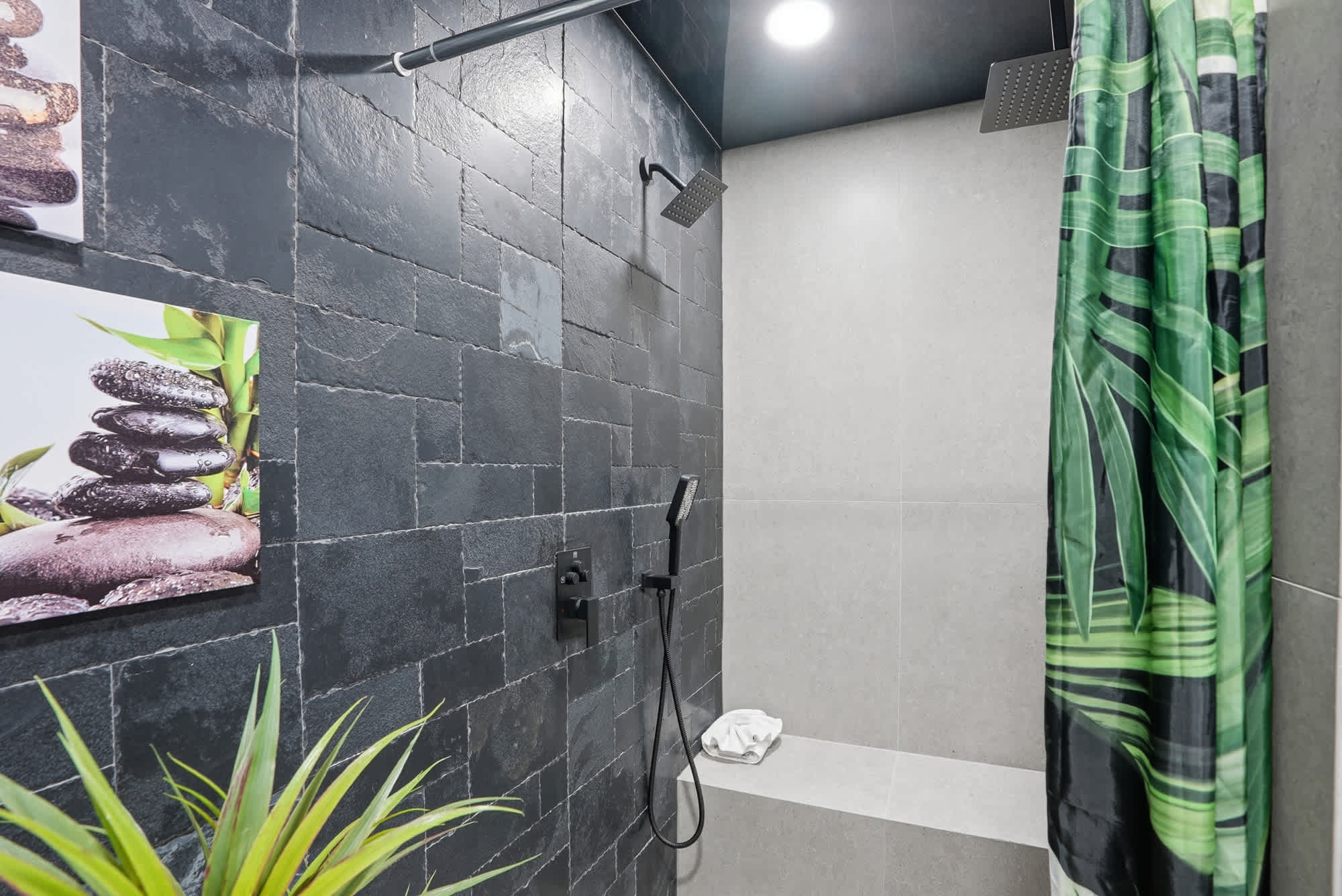 The Summit 132 – Modern shower with dark stone walls, a bench, and a plant, featuring tropical-themed shower curtain.