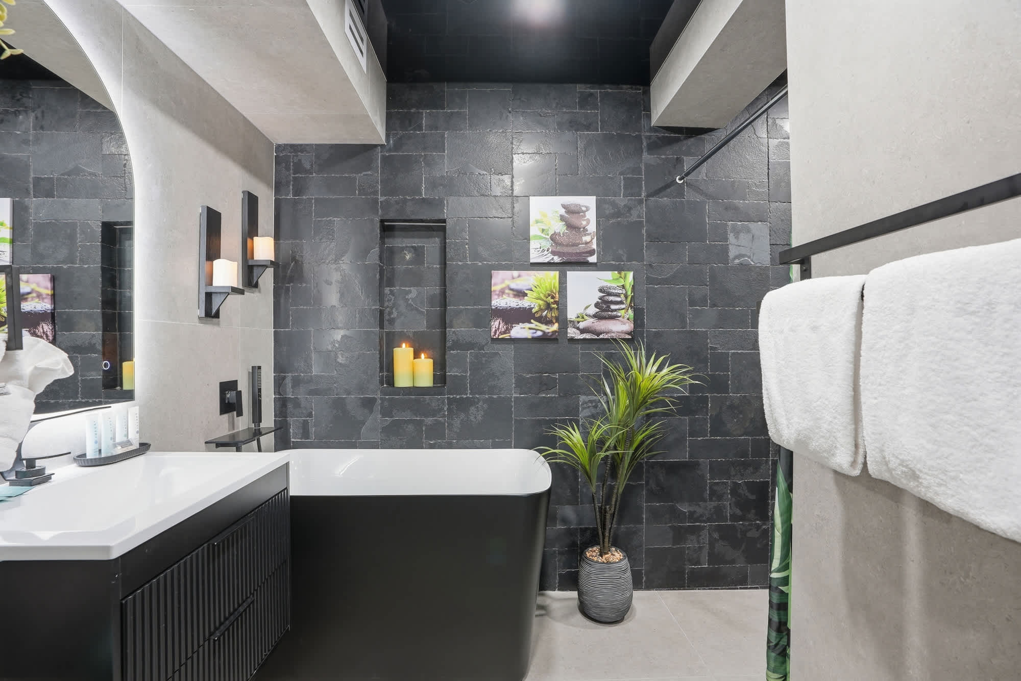 The Summit 132 – Modern bathroom with a freestanding tub, stone wall, candles, and decorative plants.