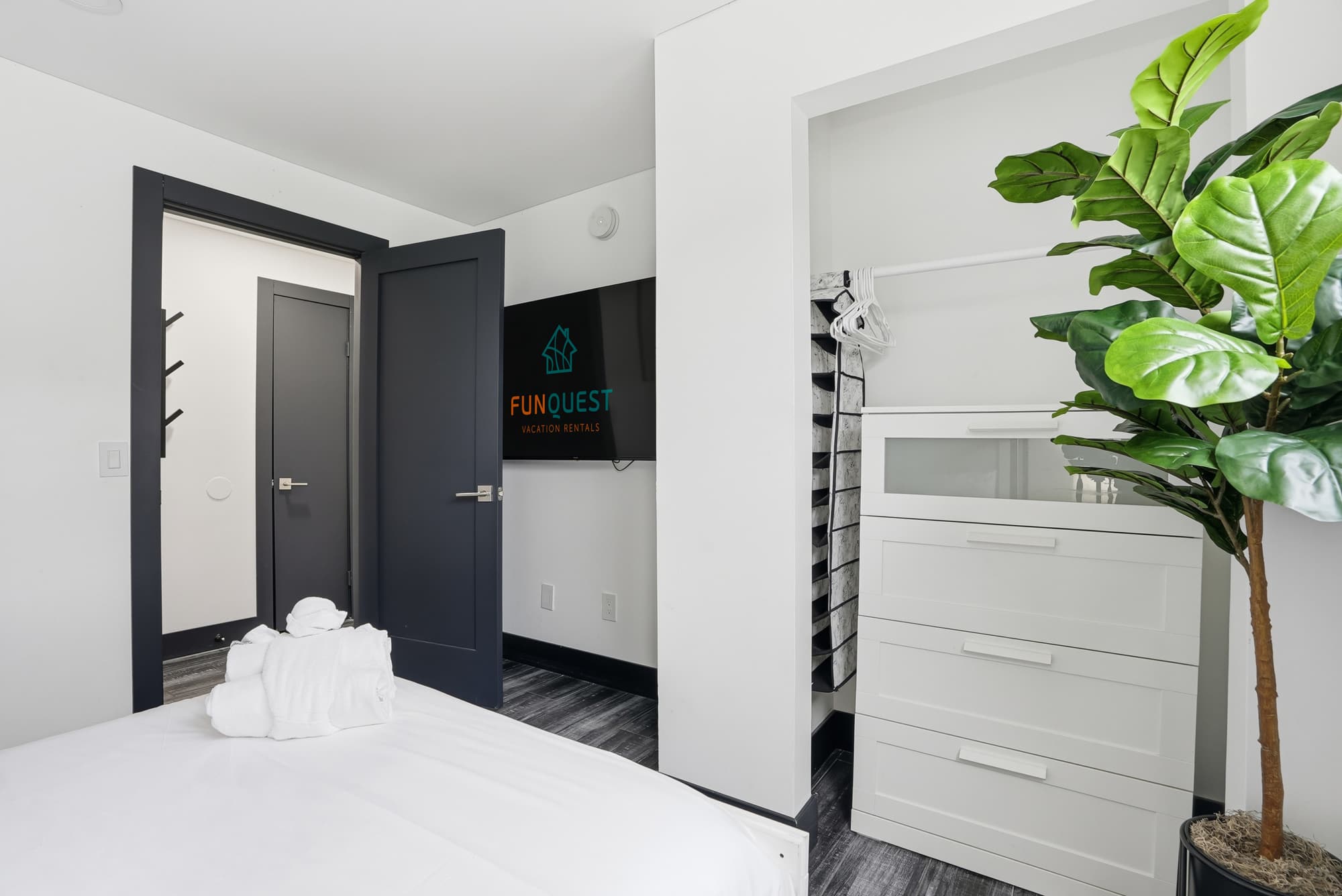 The Summit 132 – Bedroom with bed, TV, storage unit, and closet space, featuring a decorative indoor plant.