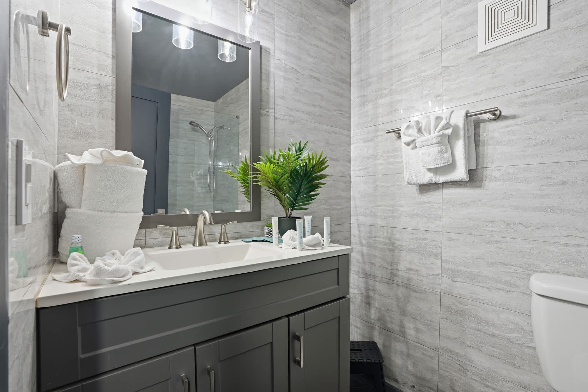 The Summit 132 – Modern bathroom with gray tile, a vanity, mirror, potted plant, and neatly arranged towels.