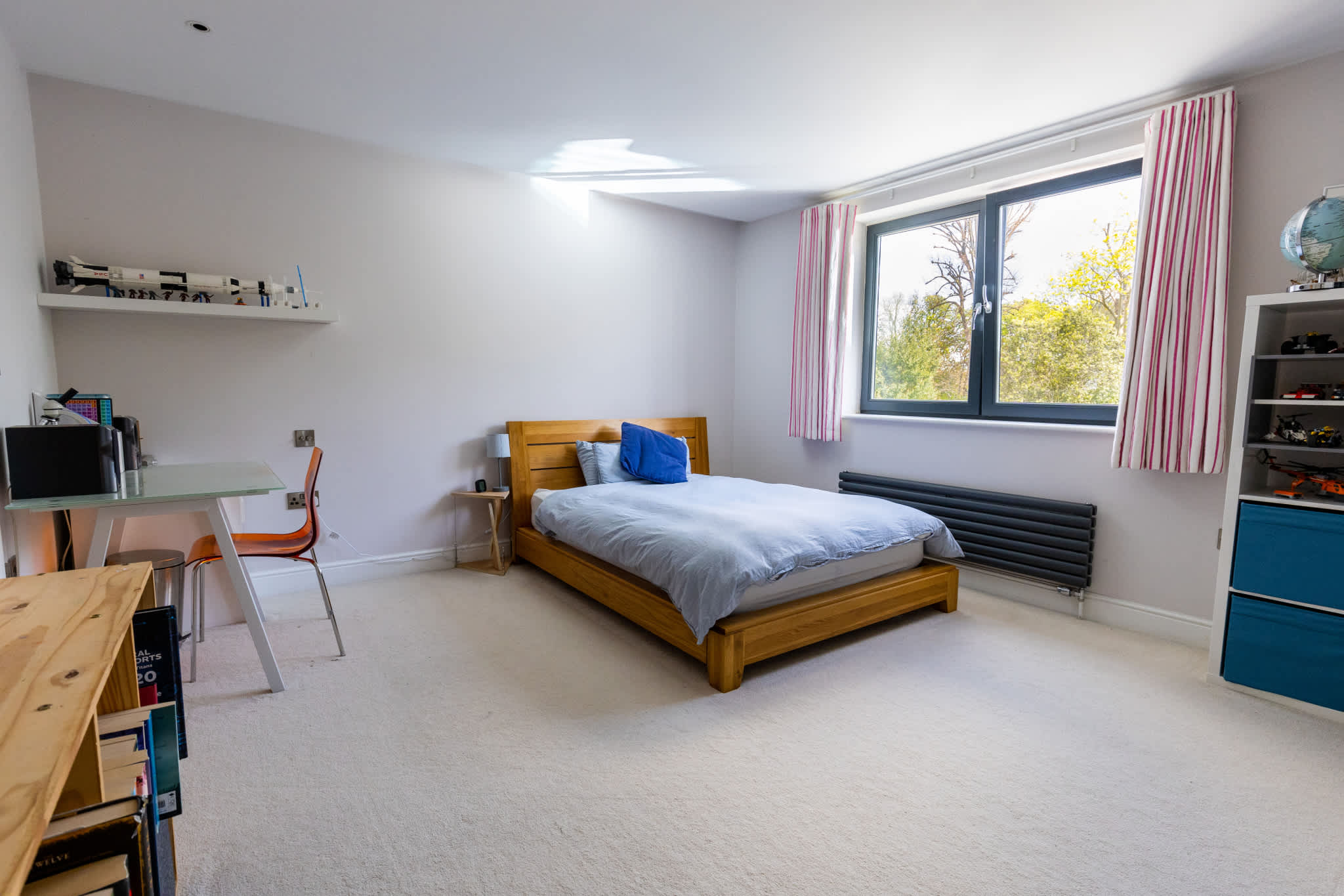 Spacious, light-filled bedroom with comfortable bed, workspace and large window for natural light.