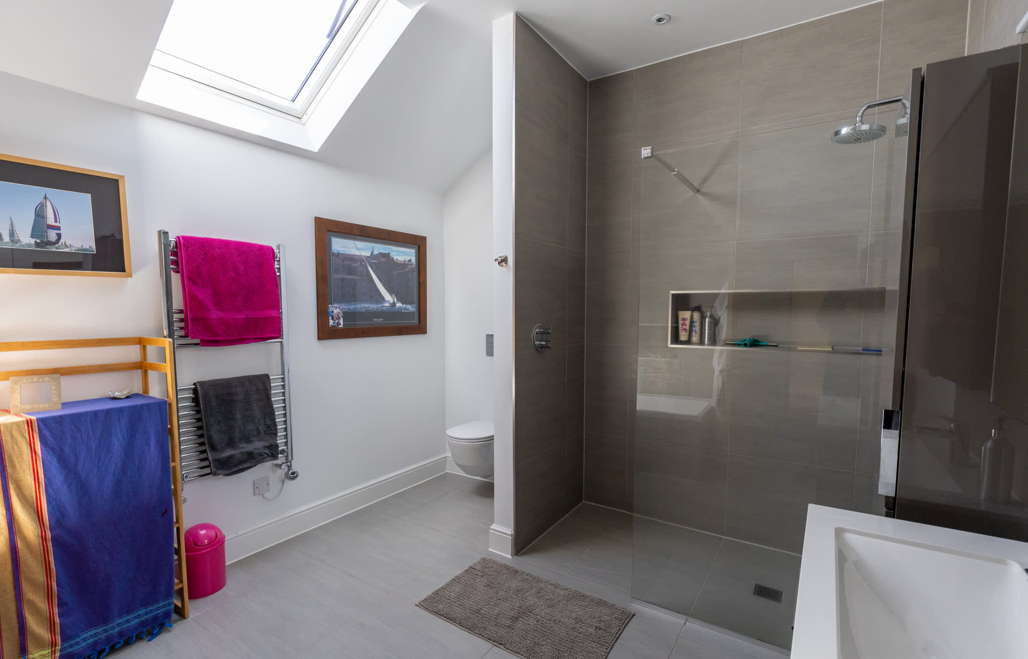 The bright, skylit bathroom serving the second floor — featuring a substantial walk-in shower with full-height grey tiles, and heated towel rail.