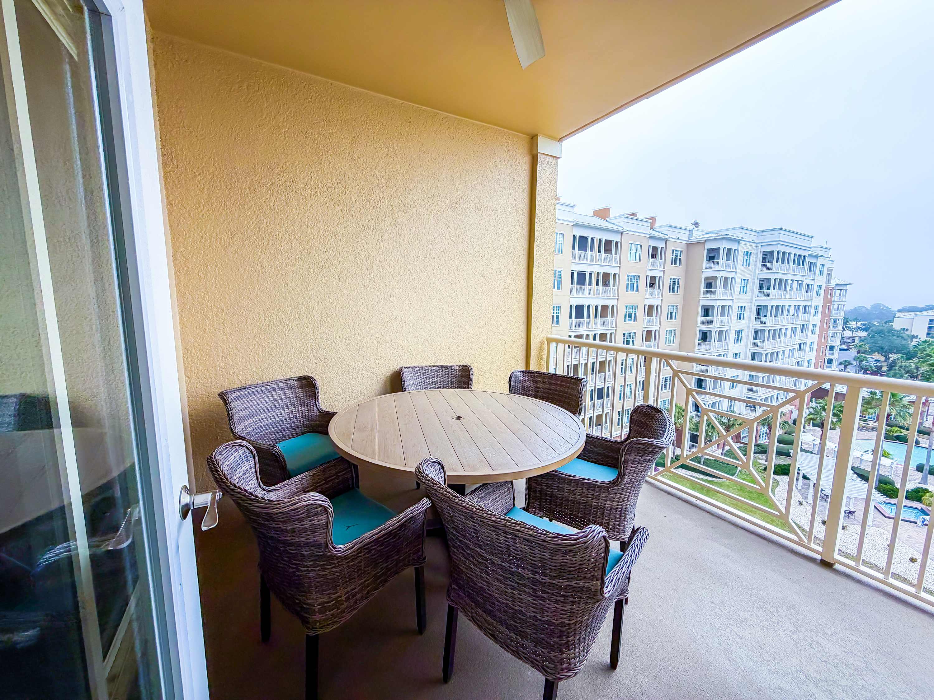 Marriott 3707 – Balcony with round table and six chairs overlooking a building and pool area.