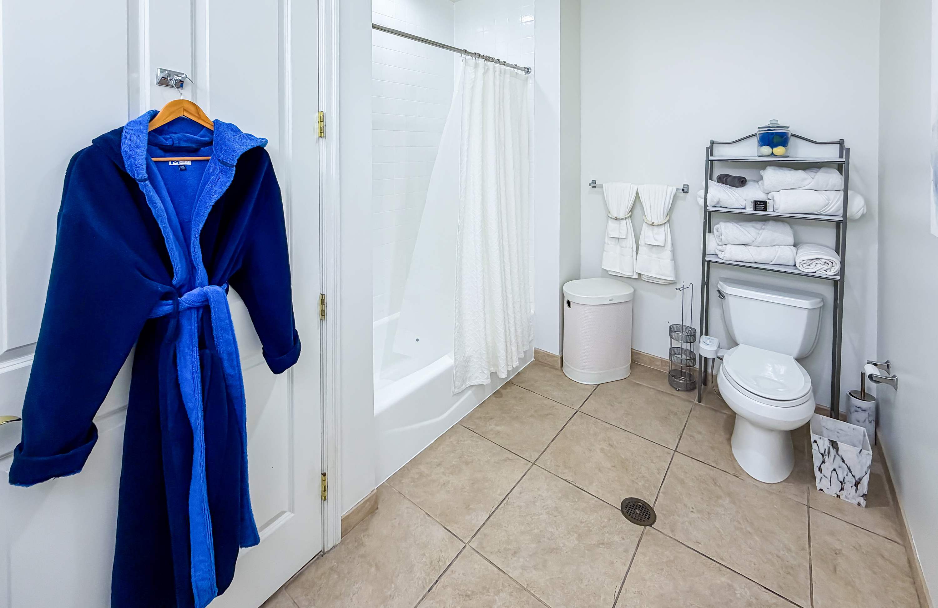 Marriott 3707 – Bathroom featuring a hanging blue robe, shower, towels, and a toilet on tiled floor.