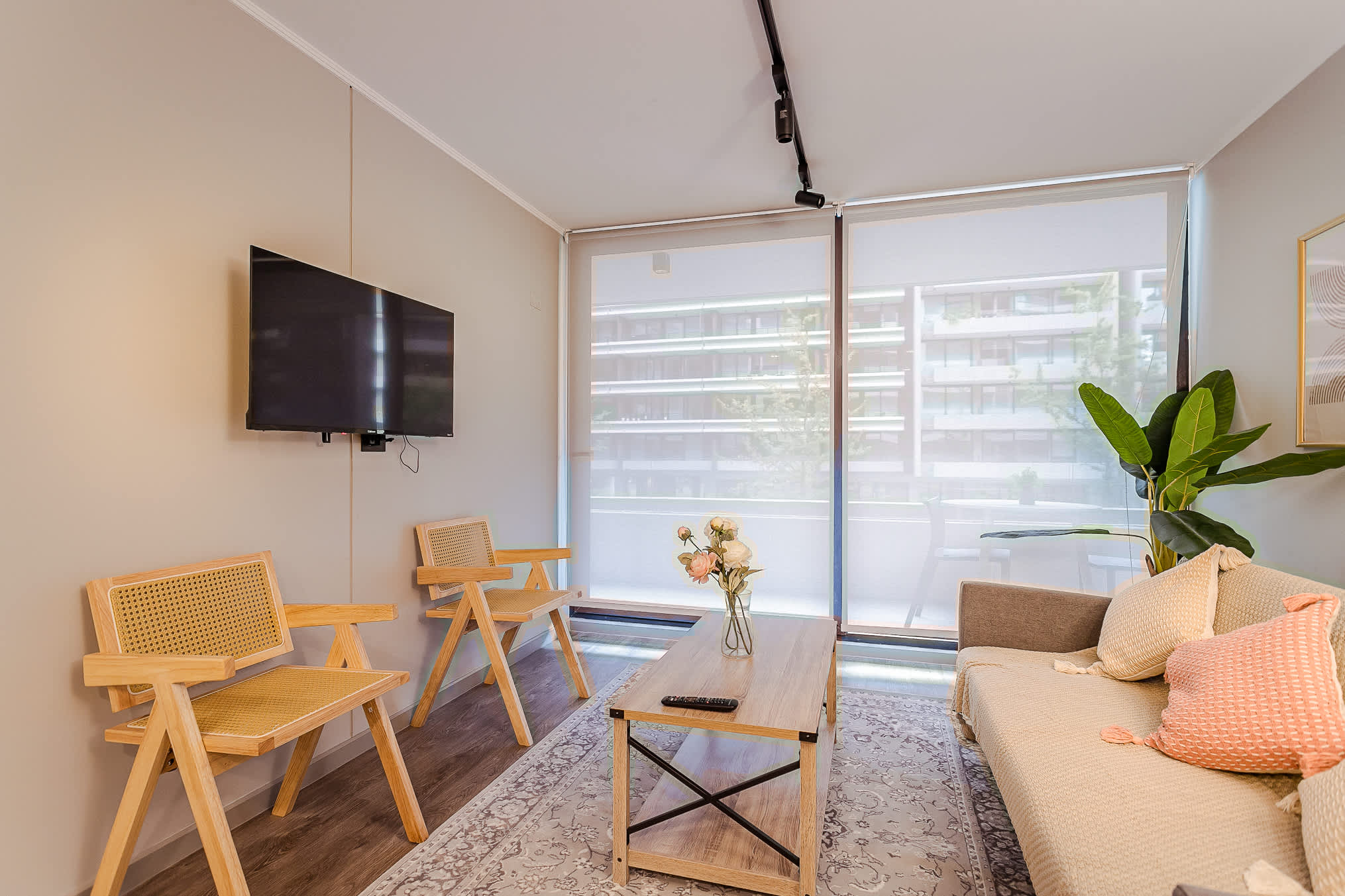Private living room with floor-to-ceiling windows, woven wood armchairs, a comfortable sofa, and a leafy indoor plant.