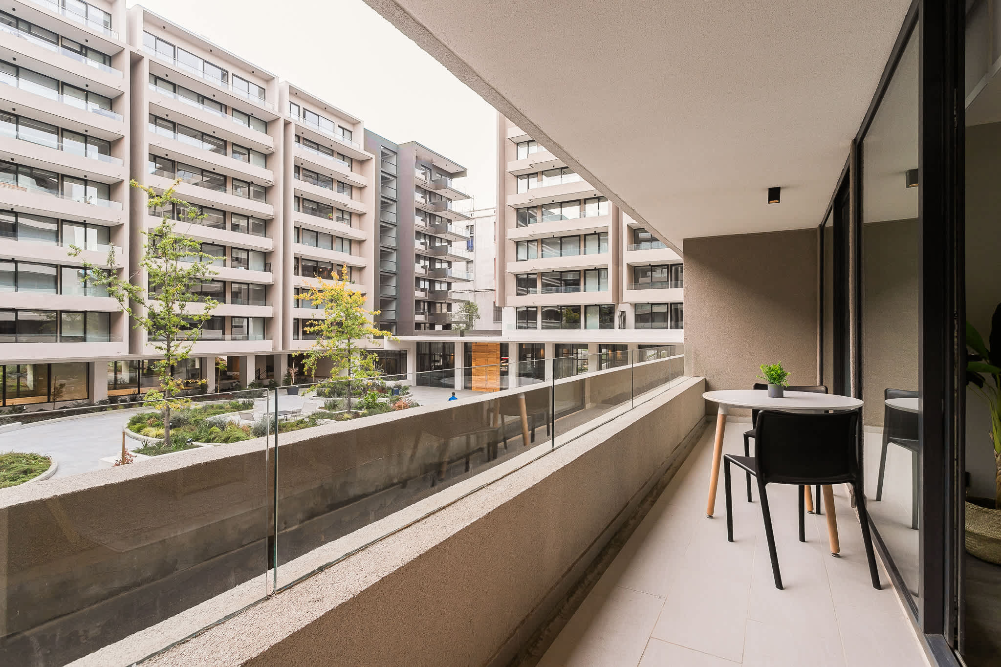 Private balcony with a café table, glass railing, and views over the landscaped courtyard.