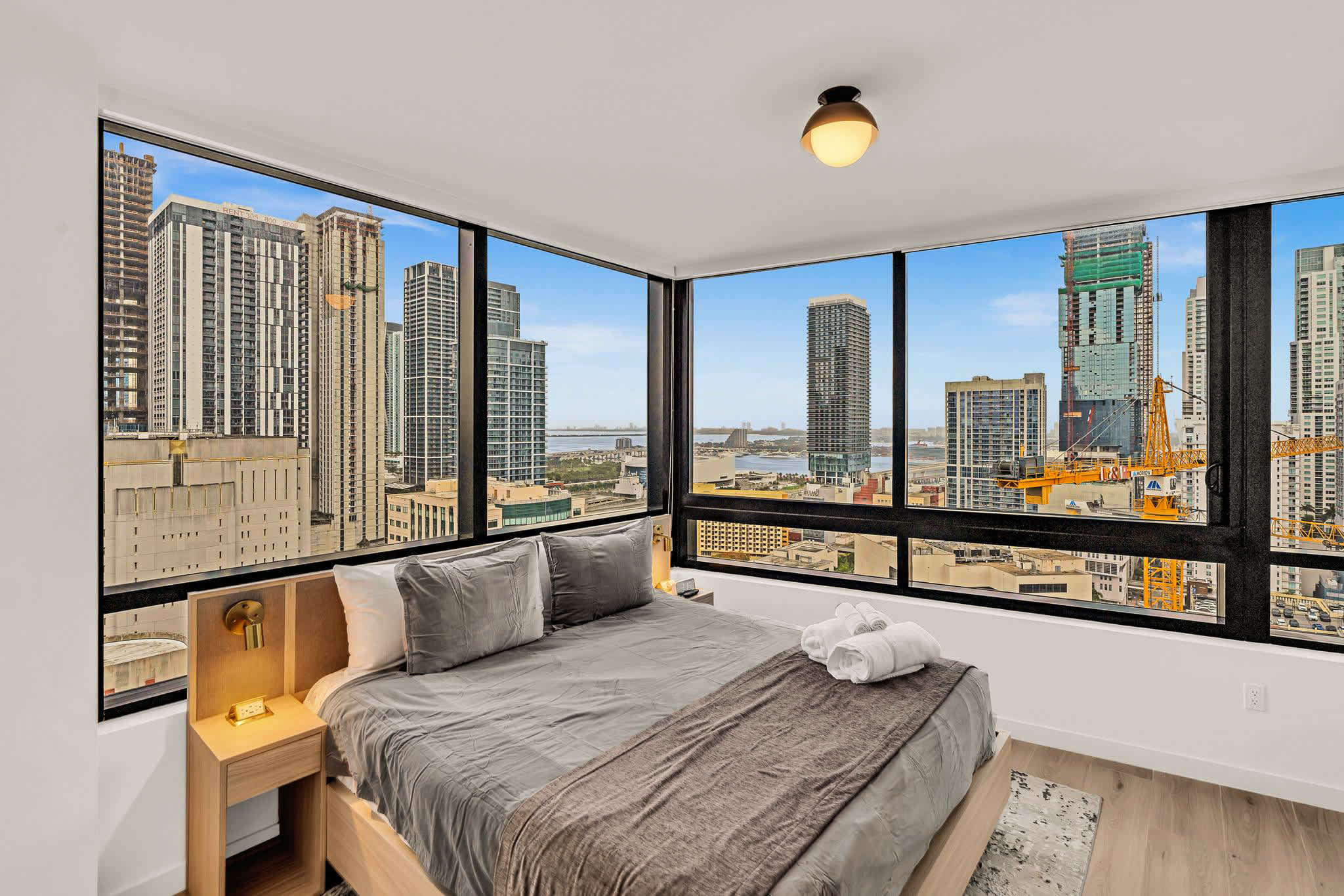 Wake up to breathtaking city views in this stylish bedroom with floor-to-ceiling windows and modern decor.