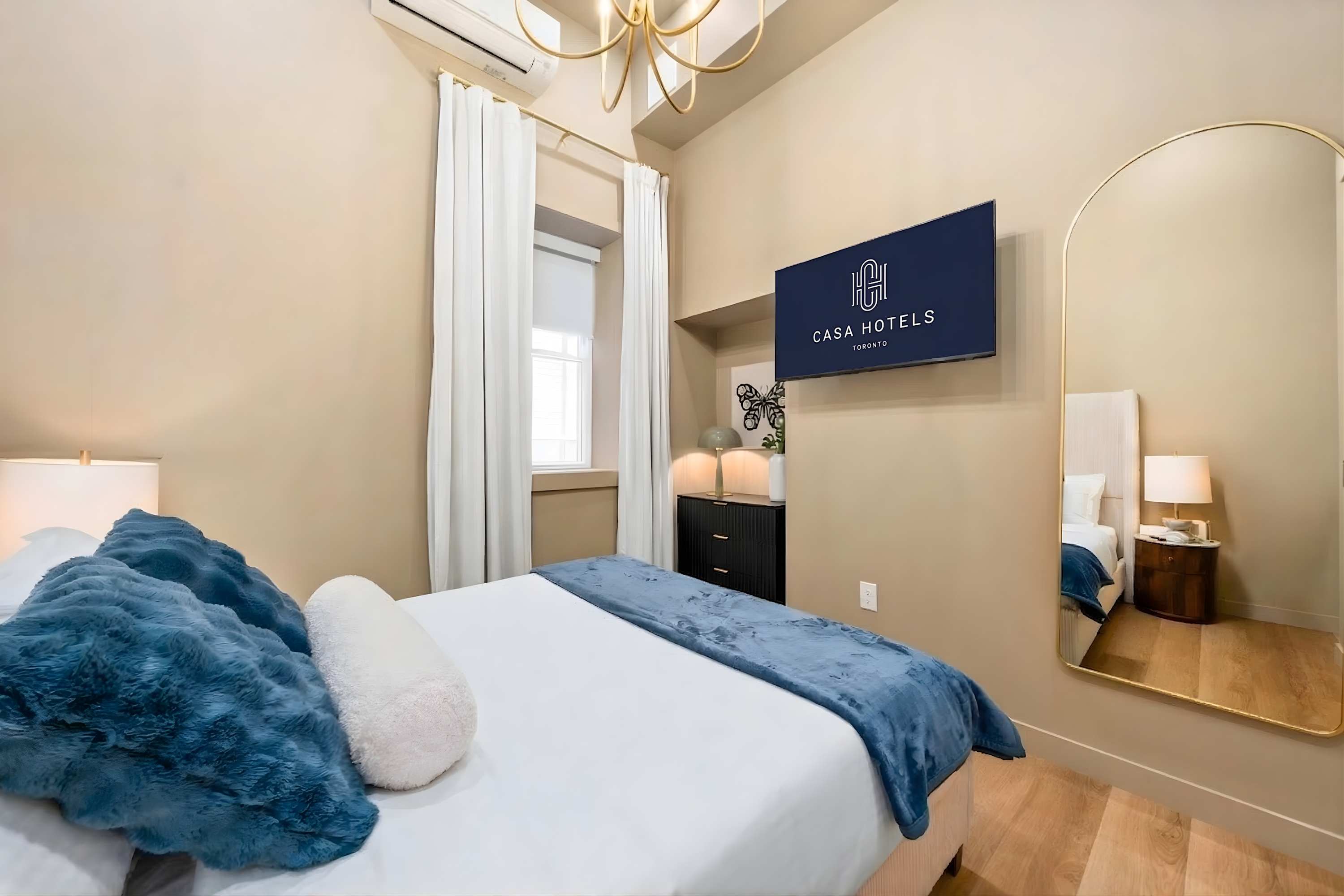 Bright bedroom with queen bed, mirror, and Smart TV.
