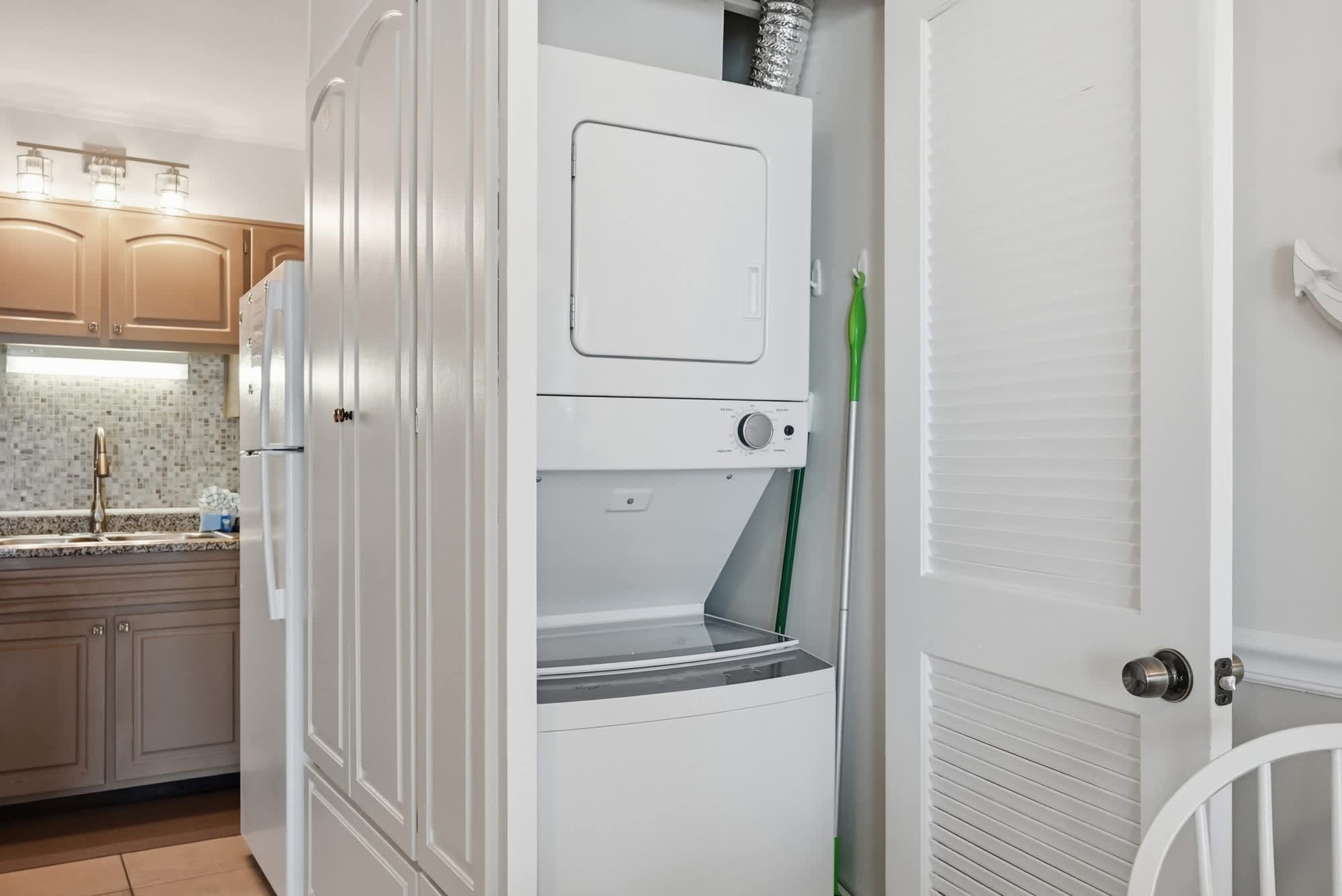 The Summit 419 – Laundry area featuring a stacked washer and dryer next to a white door and kitchen appliances.