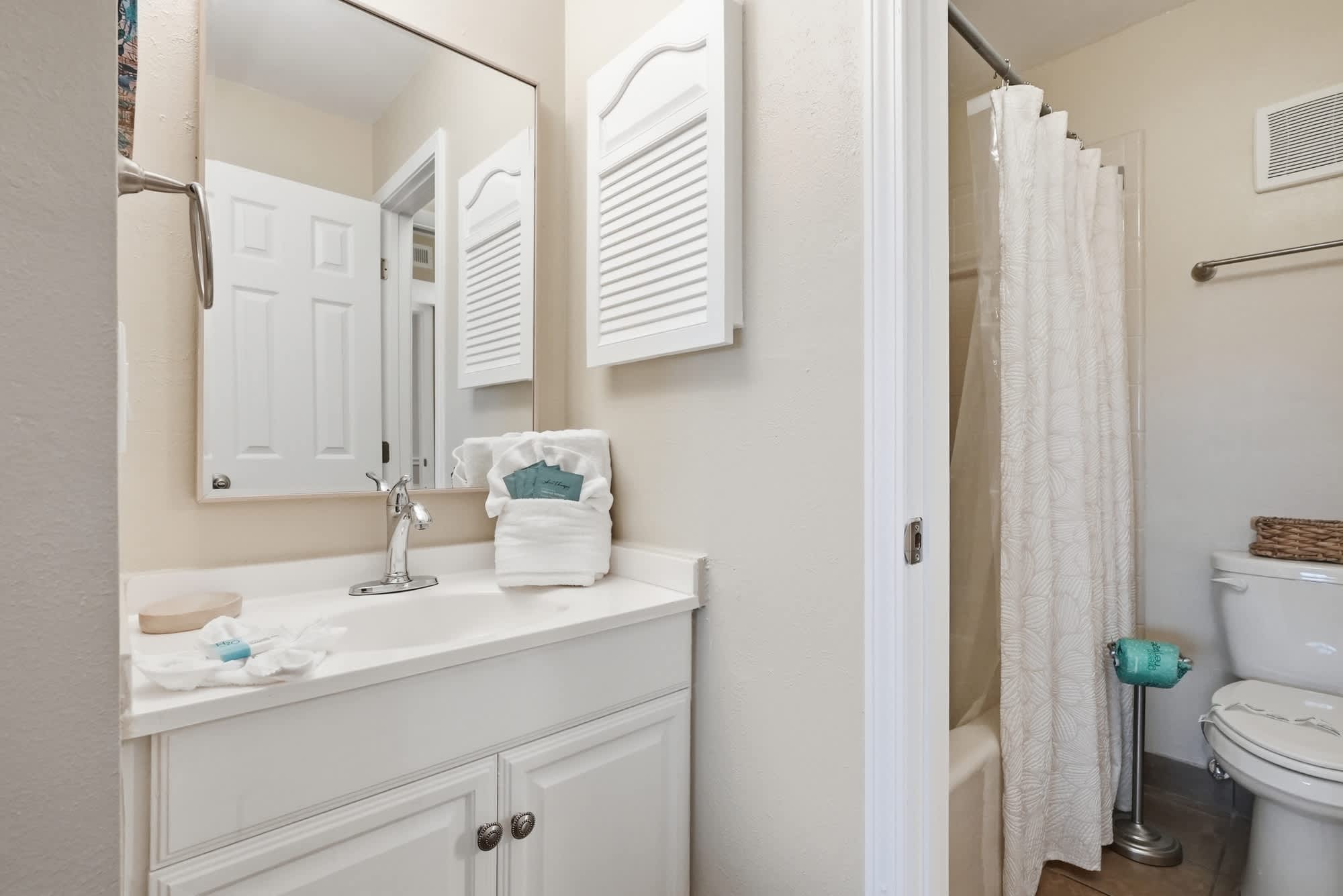 The Summit 419 – Bathroom with white cabinetry, sink, large mirror, and shower curtain.
