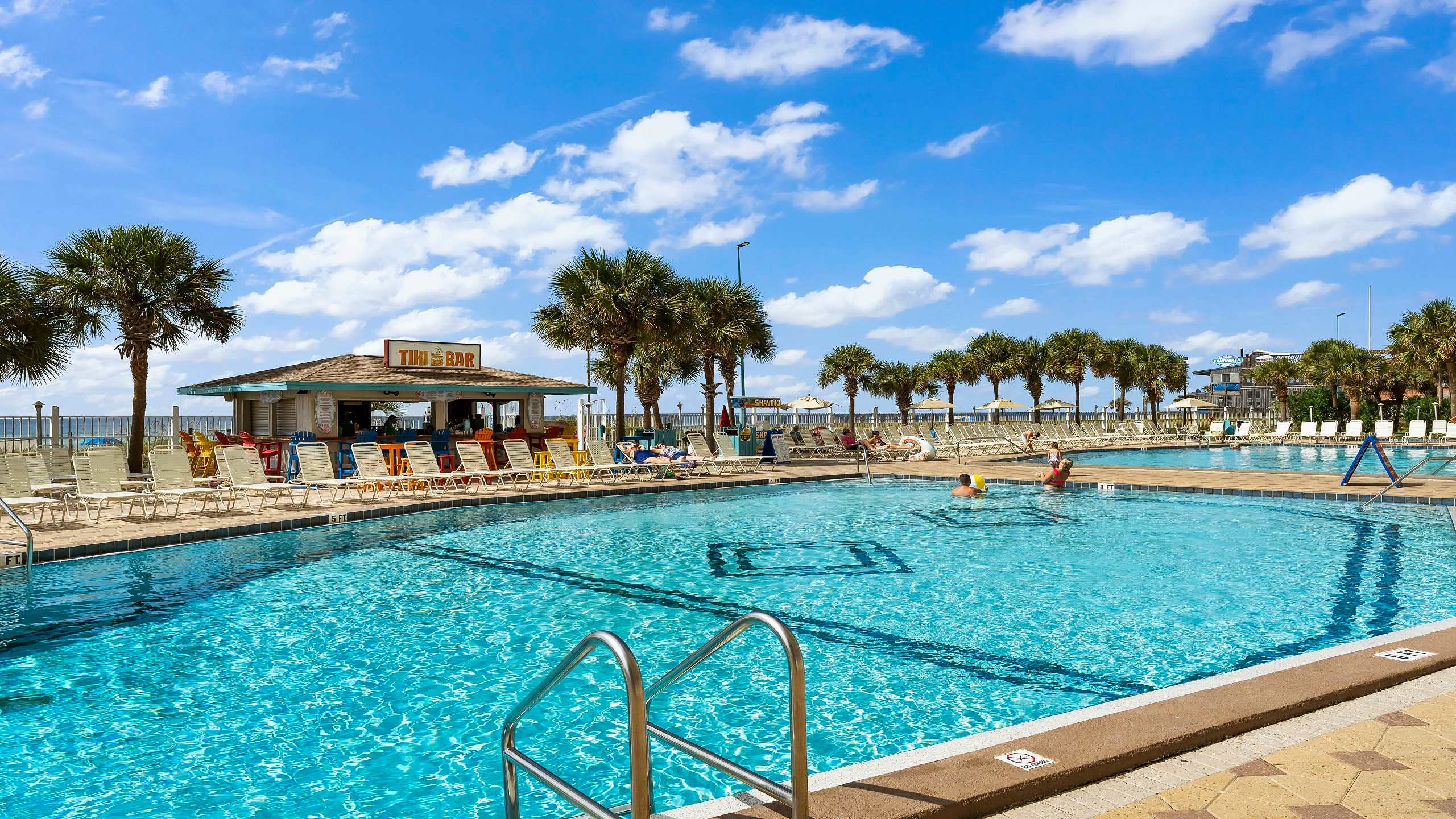 The Summit 419 – Outdoor pool area with tiki bar, lounge chairs, and palm trees under a blue sky.
