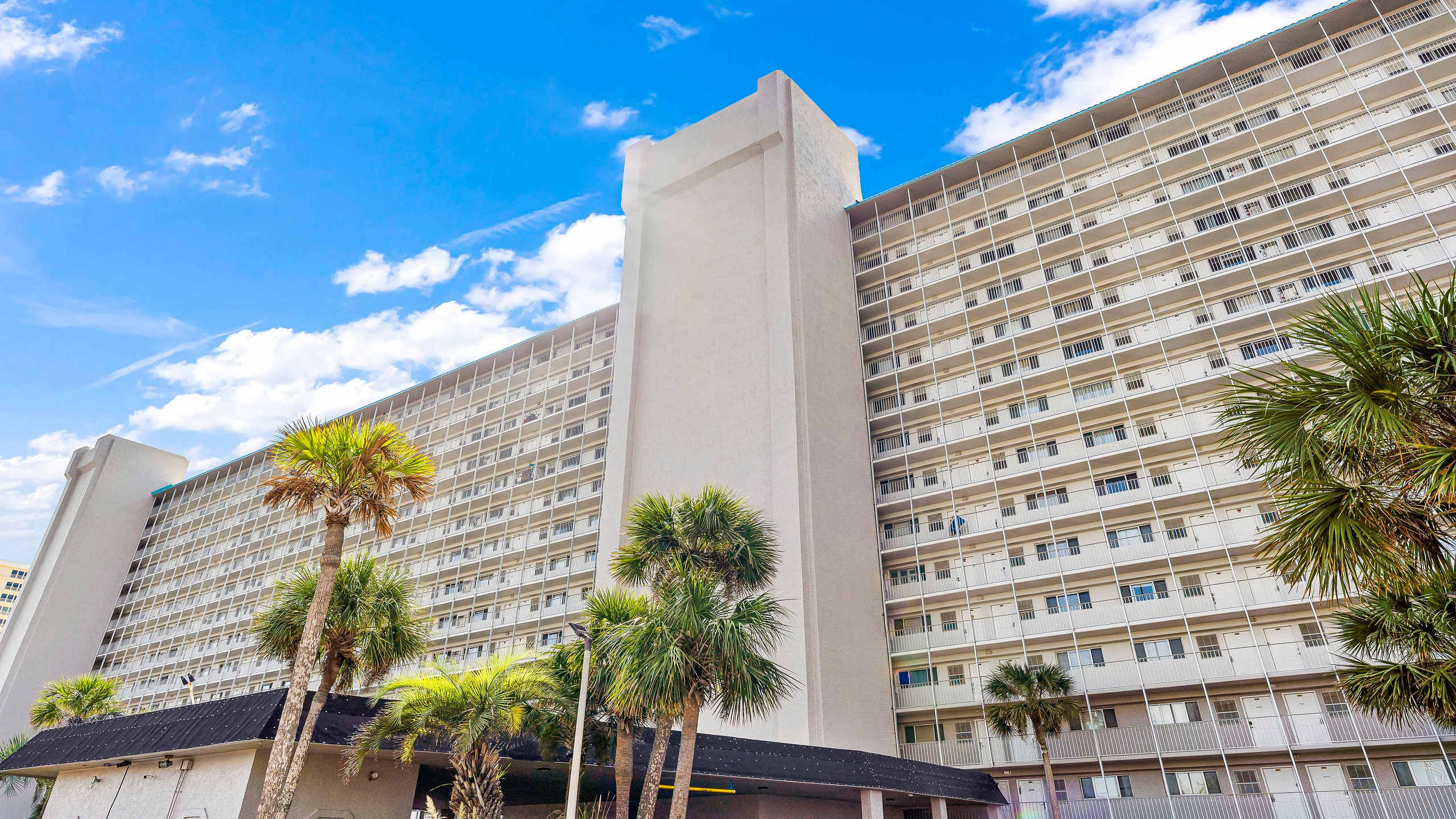 The Summit 419 – Tall, white beachside building with palm trees and multiple balconies against a blue sky.