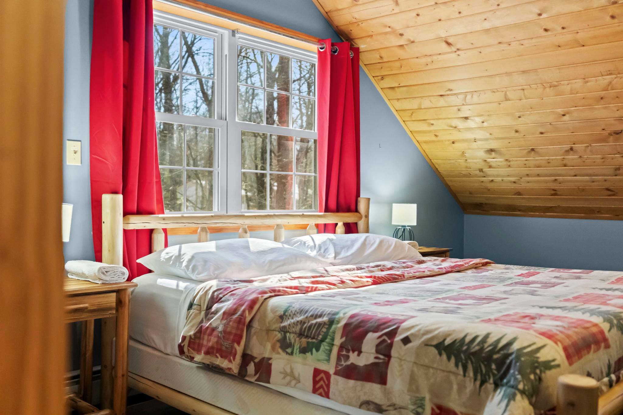 Loft-style bedroom with floral bedding and red curtains framing the windows