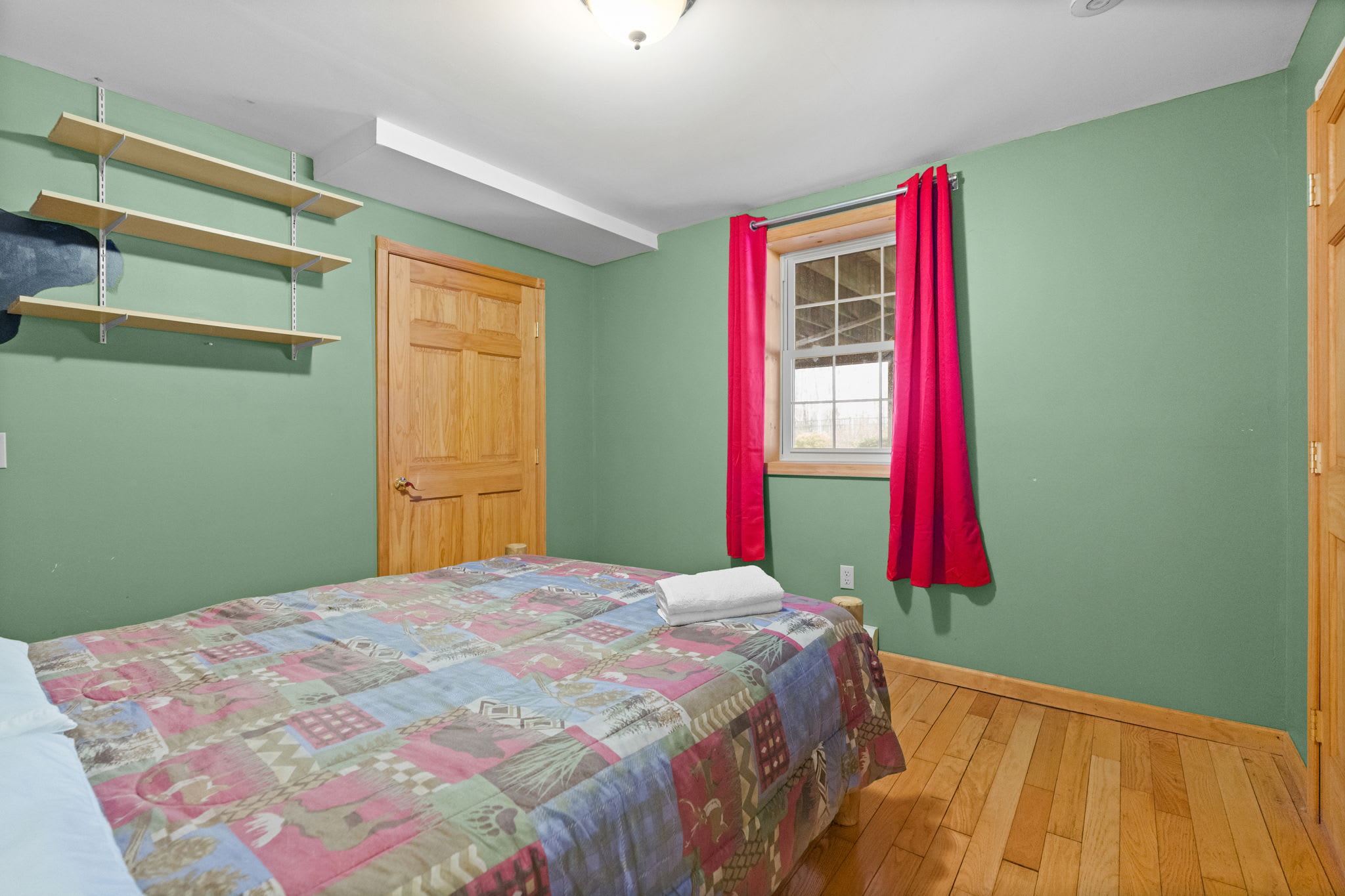 Cozy cabin bedroom with red curtains, a patchwork quilt, and golden hardwood floors