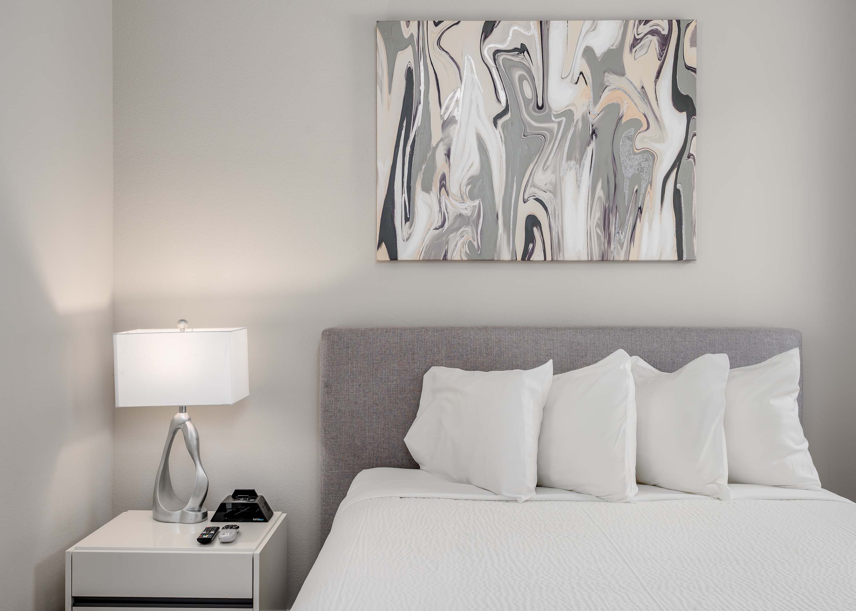 Modern bedroom with a gray upholstered headboard and abstract wall art above the bed