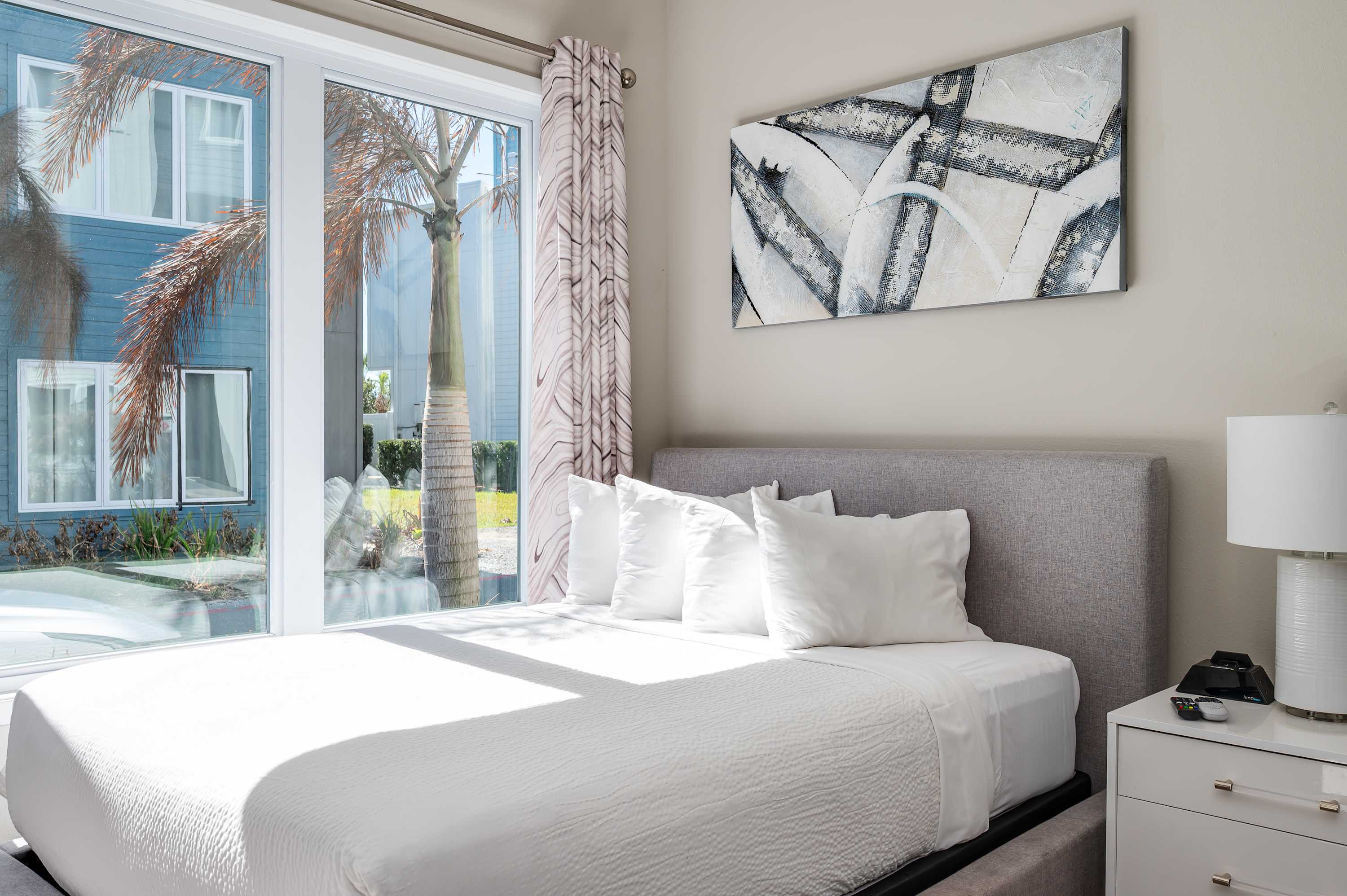 Bright bedroom with a large window overlooking palm trees and modern artwork above the bed.