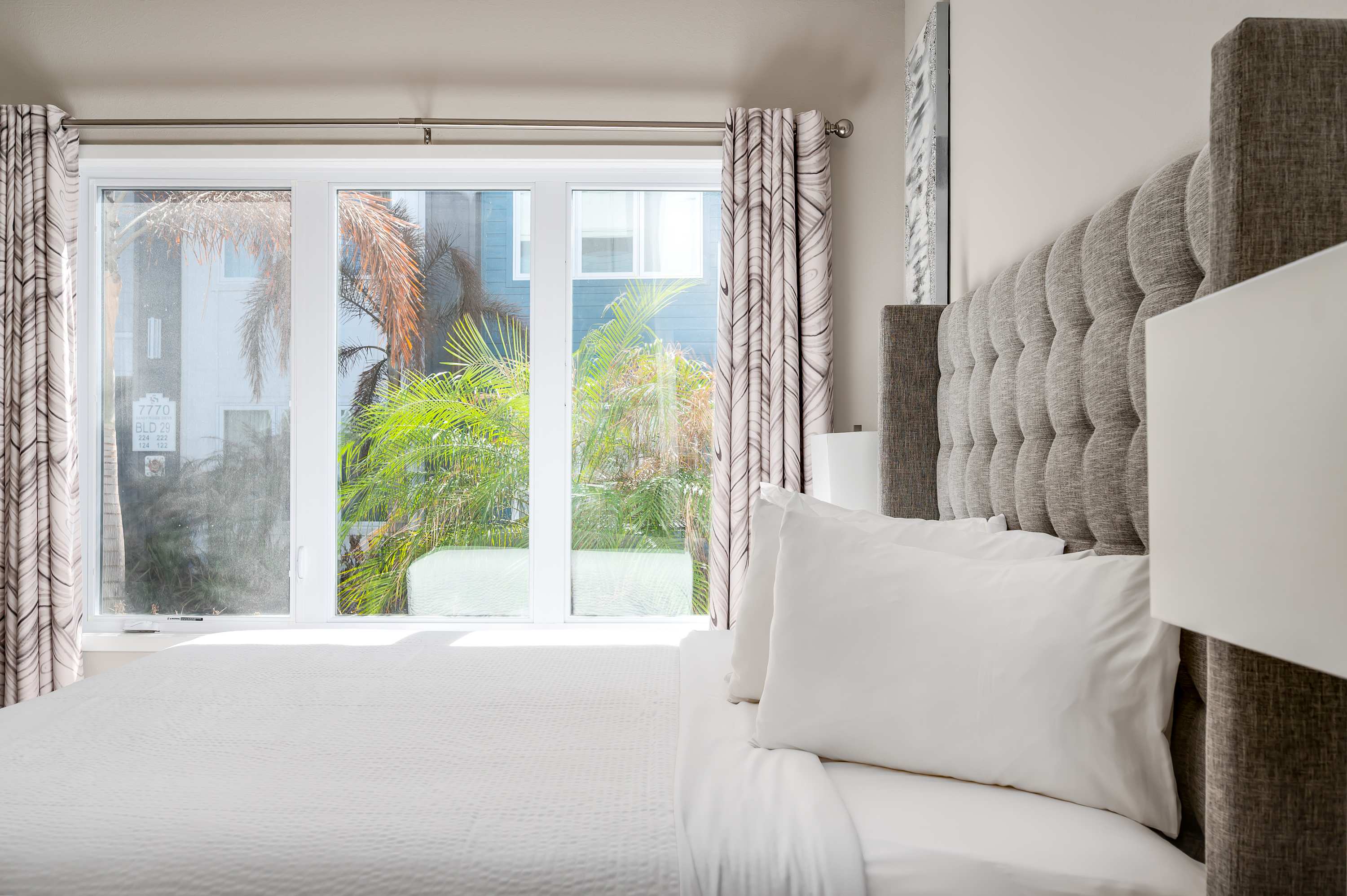 Bright bedroom with a textured gray headboard and large window overlooking greenery.