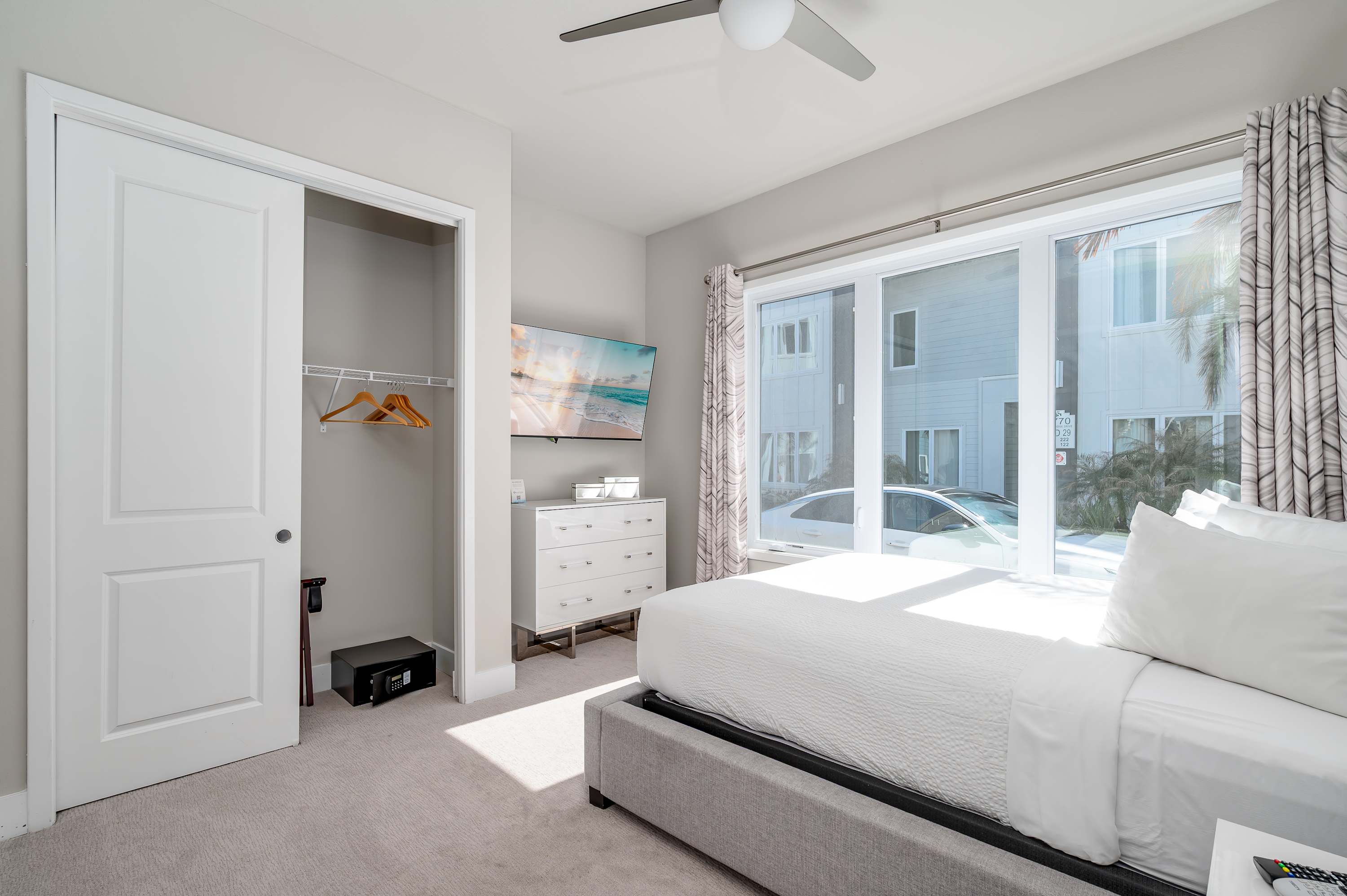 Bright bedroom with large windows, a ceiling fan, and a wall-mounted television for relaxing stays.