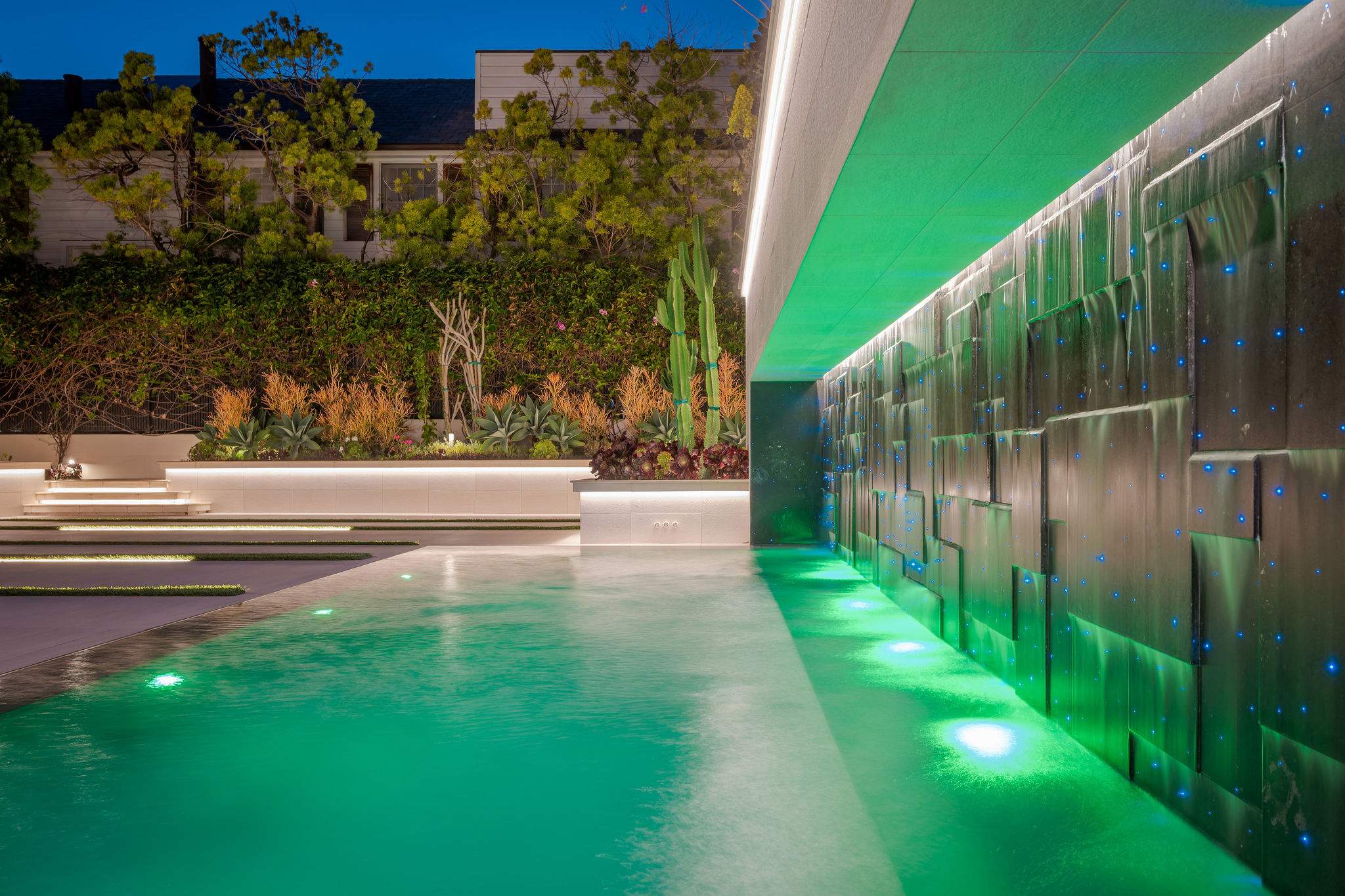 Sit beside the illuminated water-wall, with the pool running along its edge.