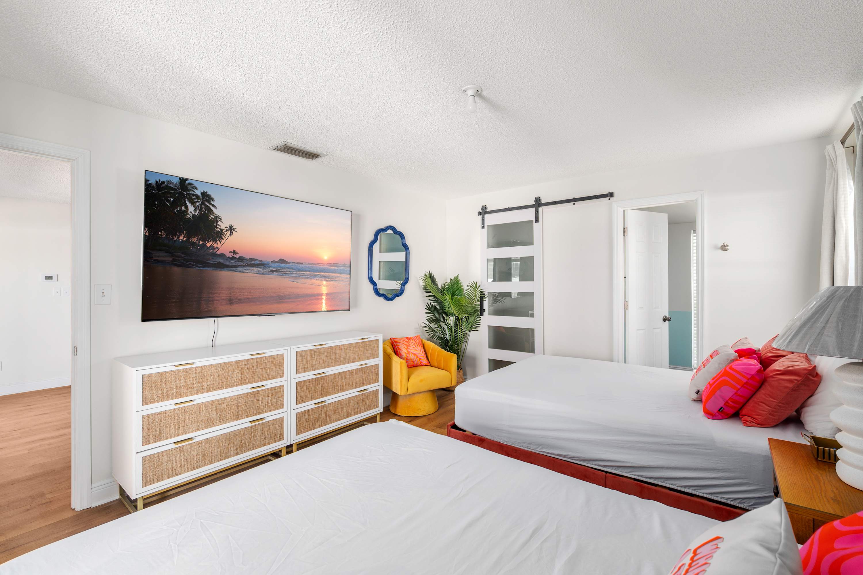 Bright bedroom with two beds, a large wall-mounted TV, and a cozy yellow armchair.