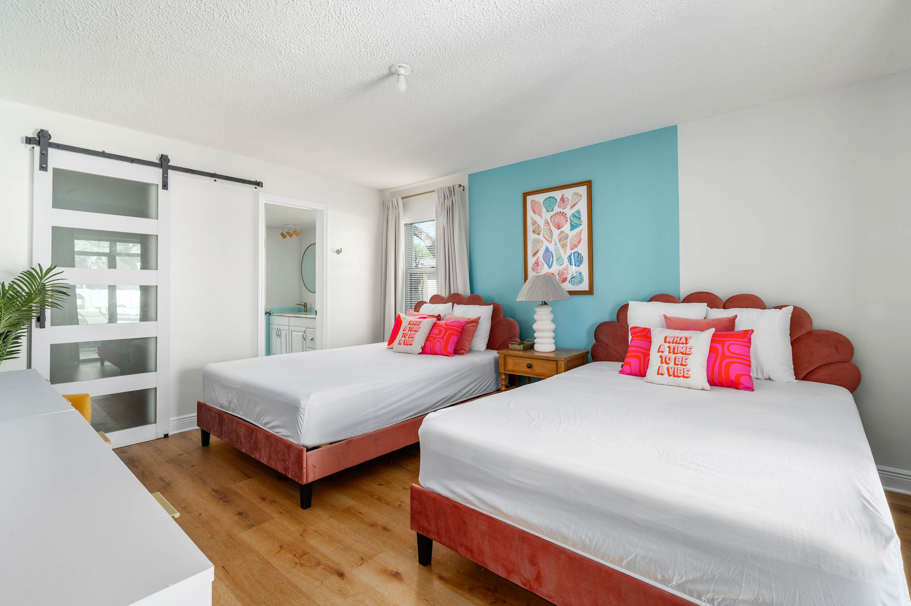 Two queen beds with coral velvet headboards and a bright blue accent wall create a cheerful guest room.