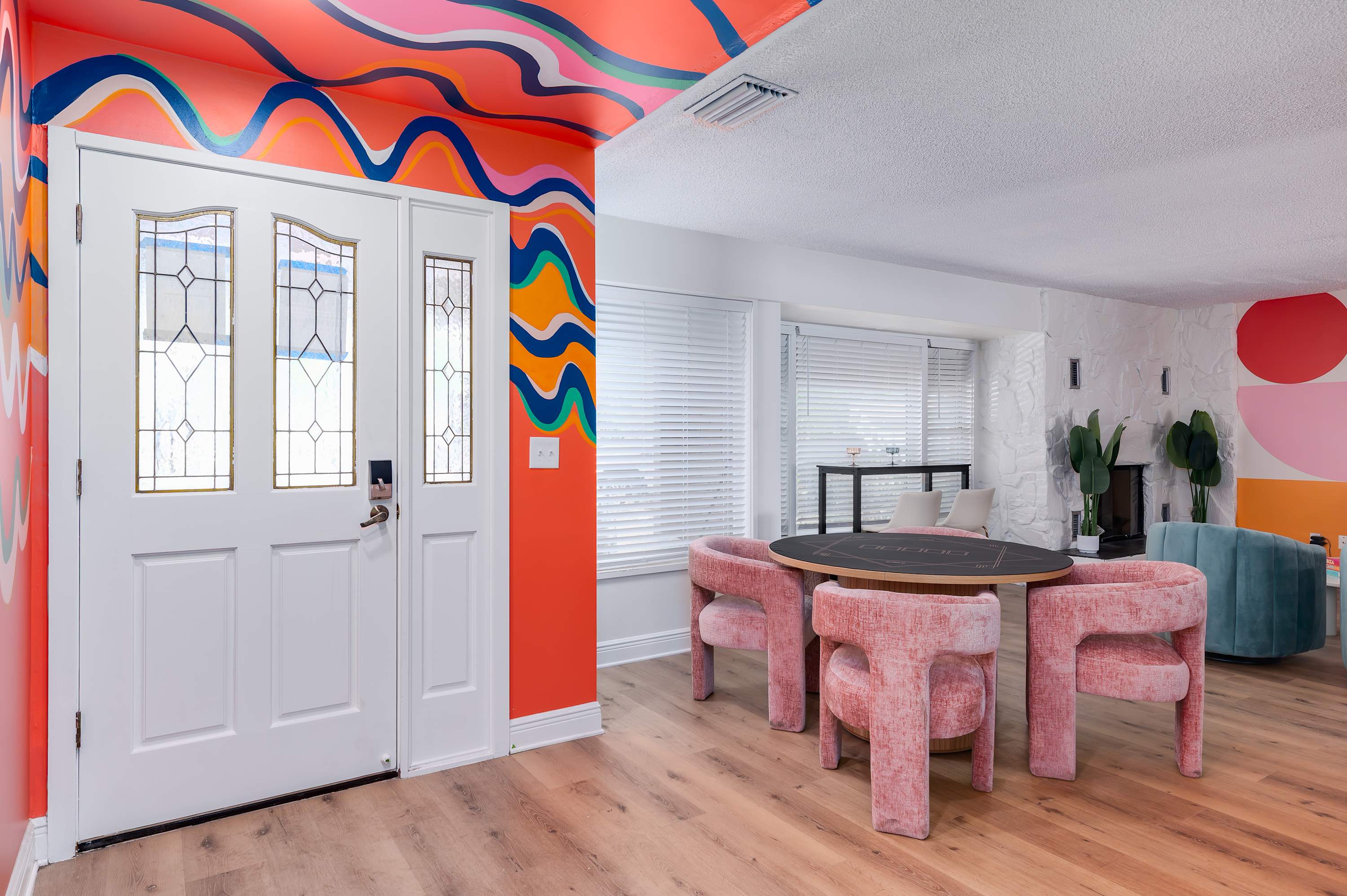 Colorful entryway with vibrant wall art leading to a modern dining area with pink velvet chairs.