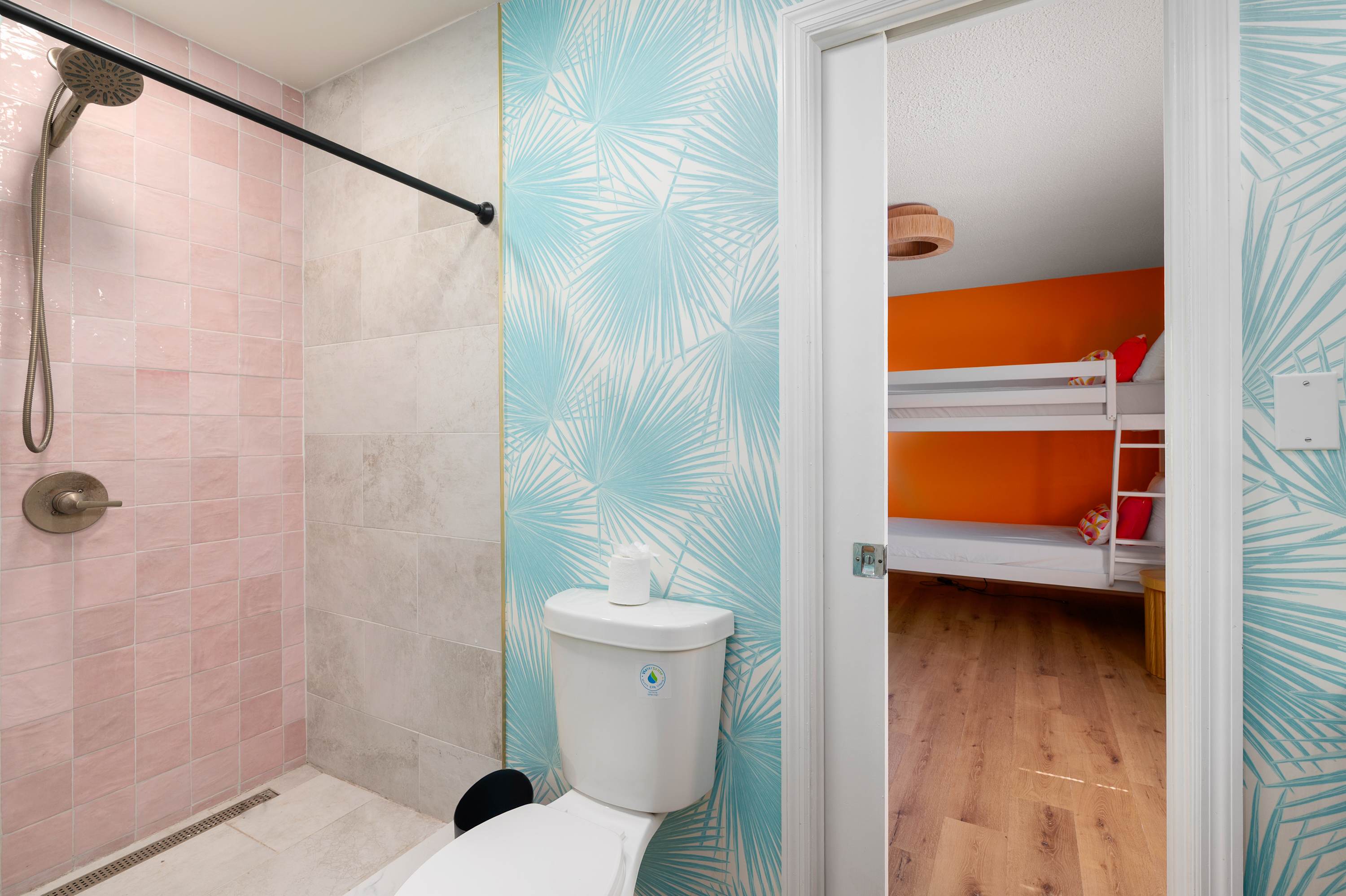 Bathroom with pink tiled shower and tropical wallpaper next to a bunk bedroom