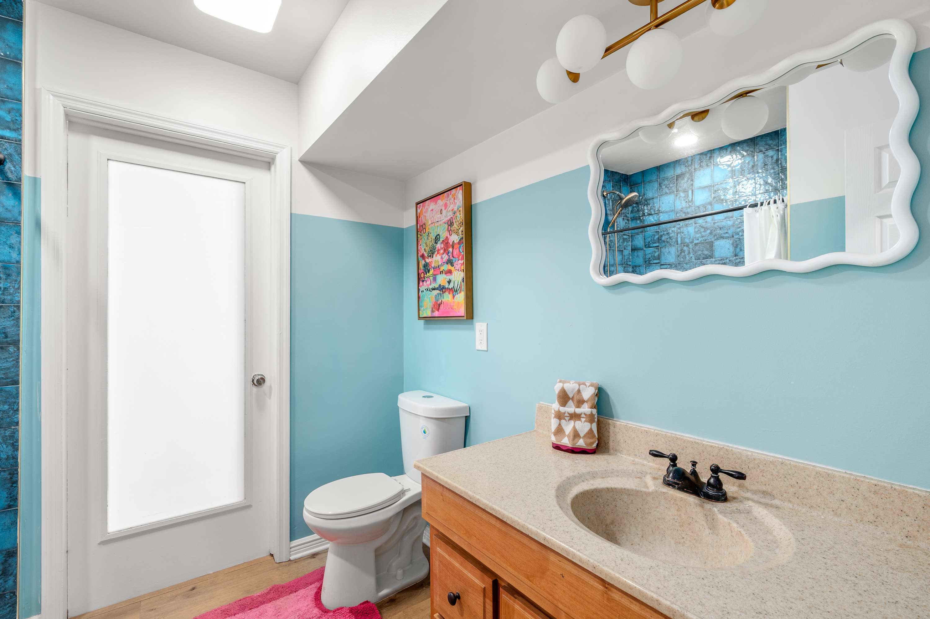 Bright bathroom with blue tiled shower and a wavy framed mirror