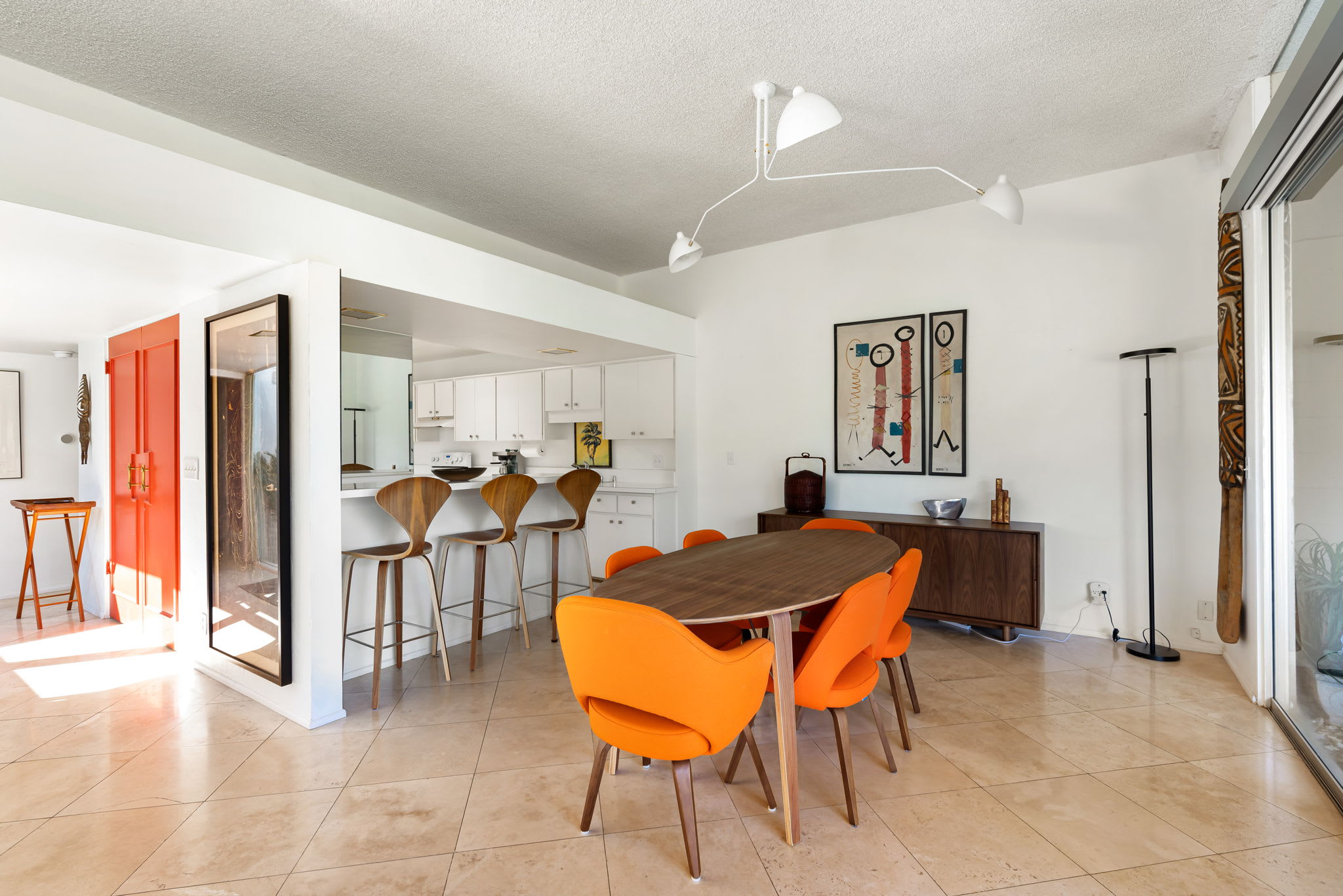Dining area with a wooden table and orange chairs beside the open kitchen.