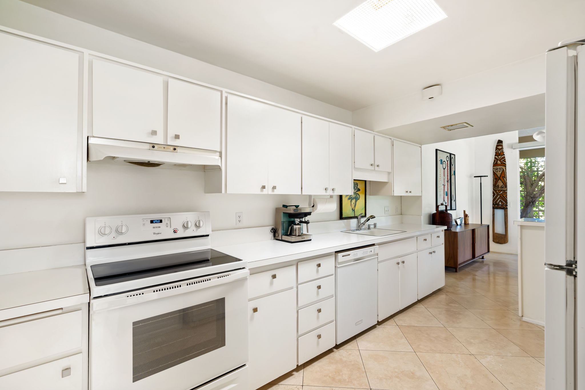White kitchen with a range, long countertop and tiled floor.