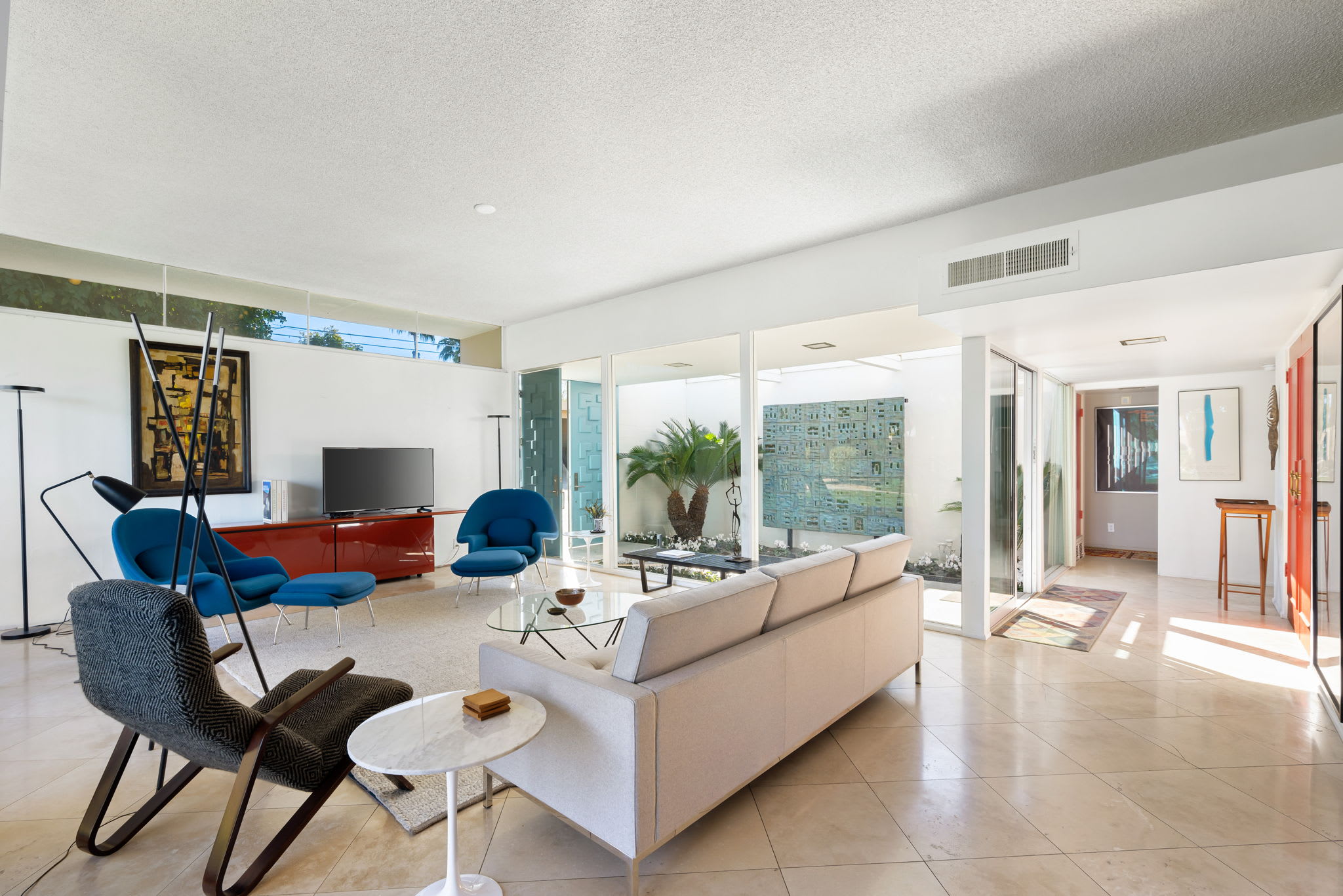Living room with a white sofa, blue chairs, television and open dining area.