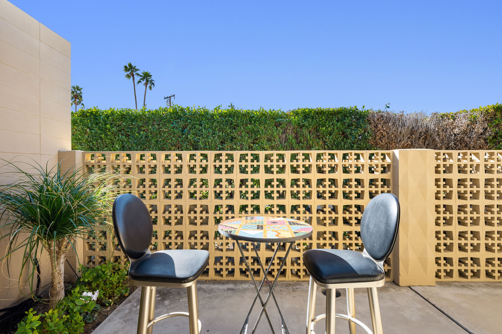 Covered porch with two chairs and a small round table beside a patterned wall.