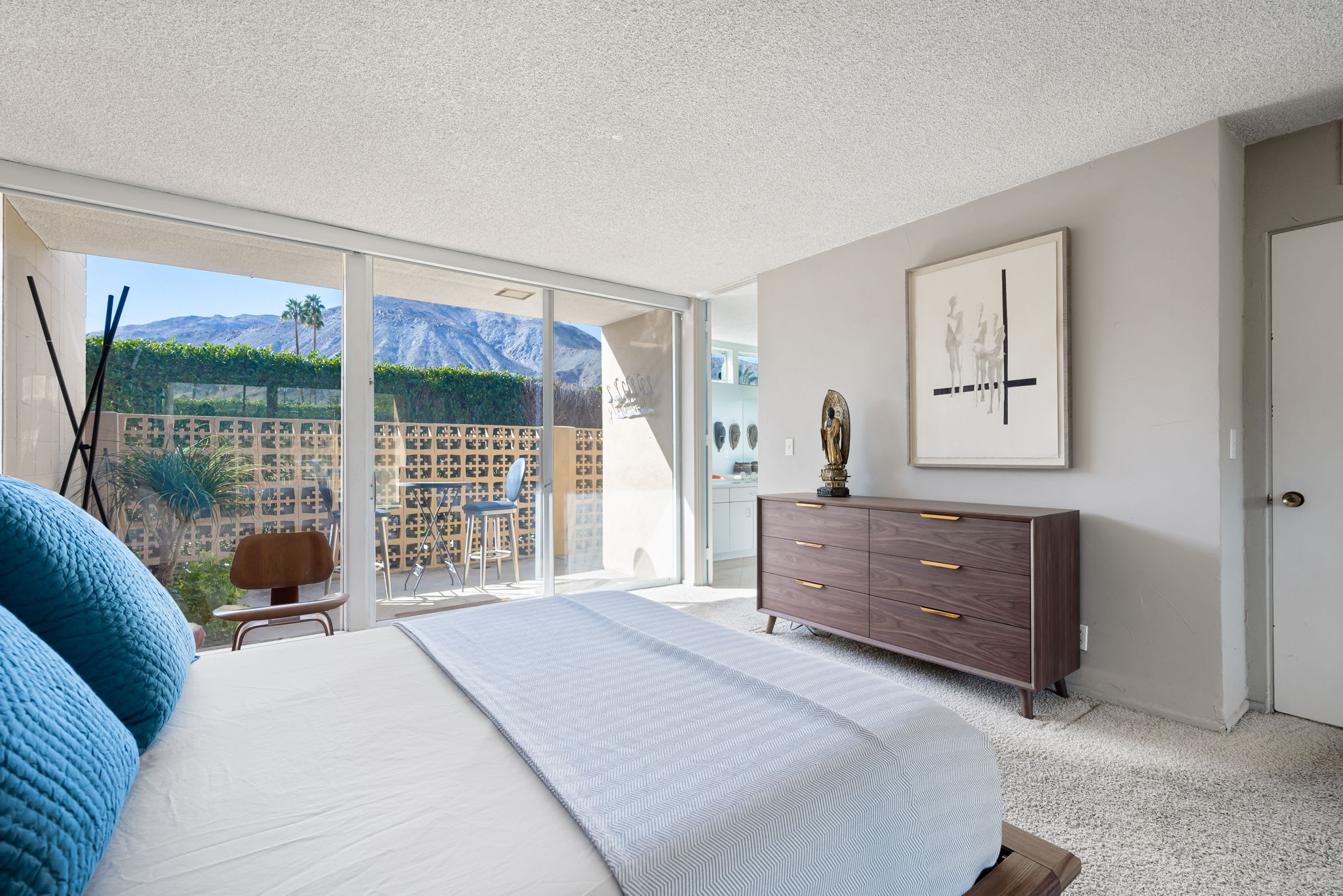 Bedroom with blue cushions, a dresser and sliding doors facing the lawn.