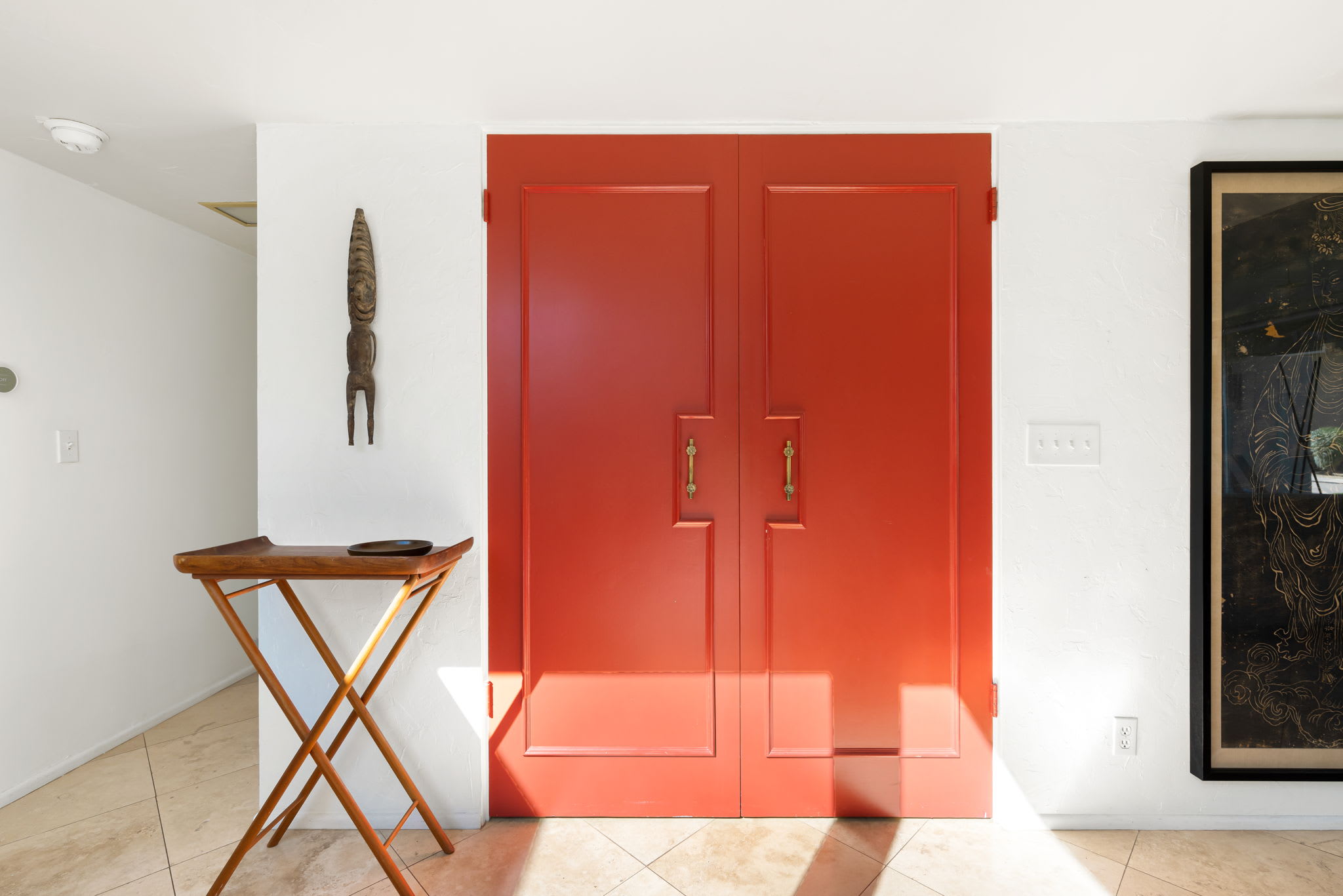 Interior entrance with red double doors, framed artwork and a side table.